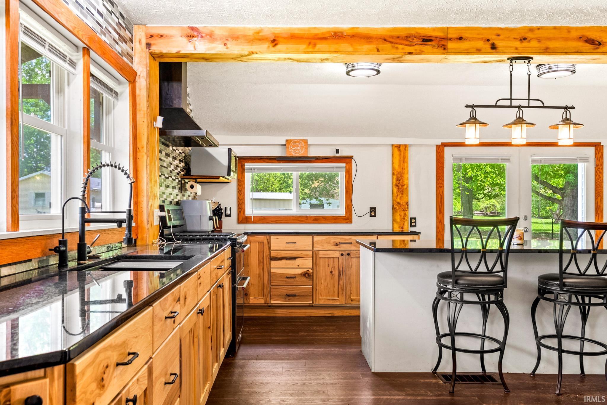 Gourmet kitchen featuring natural wood cabinetry, dark stone countertops, wood-finish flooring, a mosaic tile backsplash, and a central island with bar seating
