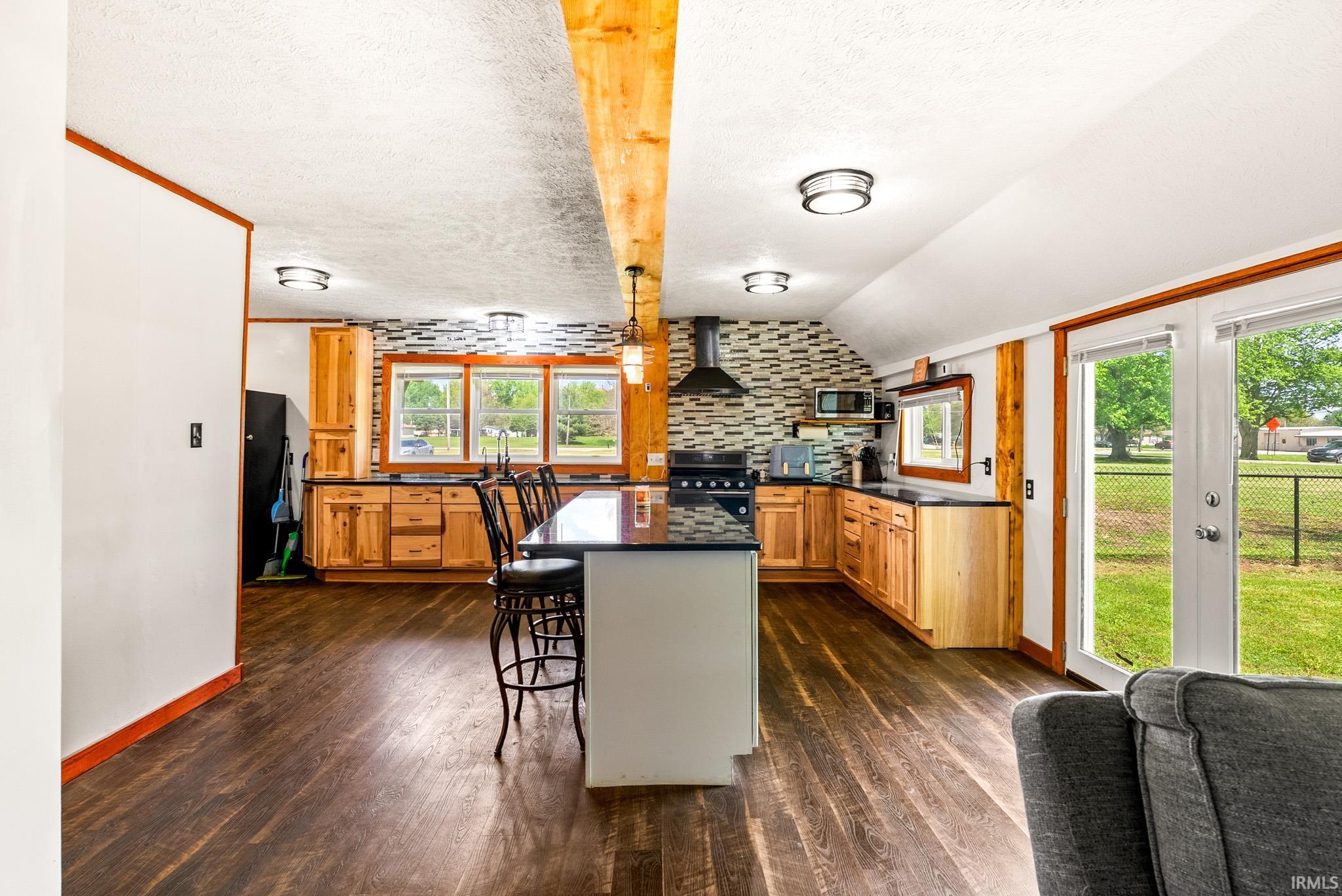 Open-concept kitchen featuring wood-finish flooring, natural wood cabinetry, a central island with countertop seating, and a geometric tiled backsplash