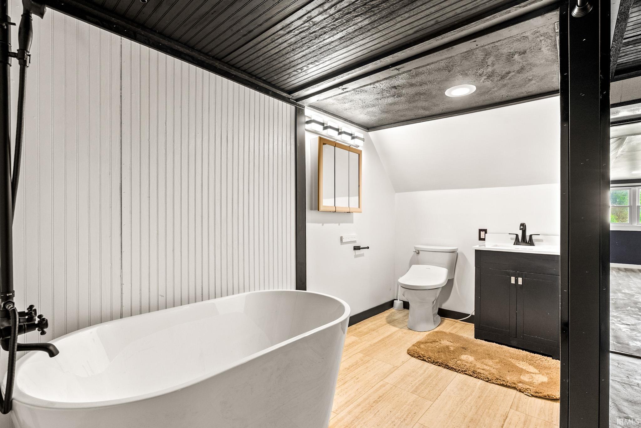 Contemporary bathroom featuring a freestanding tub with matte black fixtures, wood-finish flooring, a dark vanity with a white countertop, and a medicine cabinet with integrated lighting