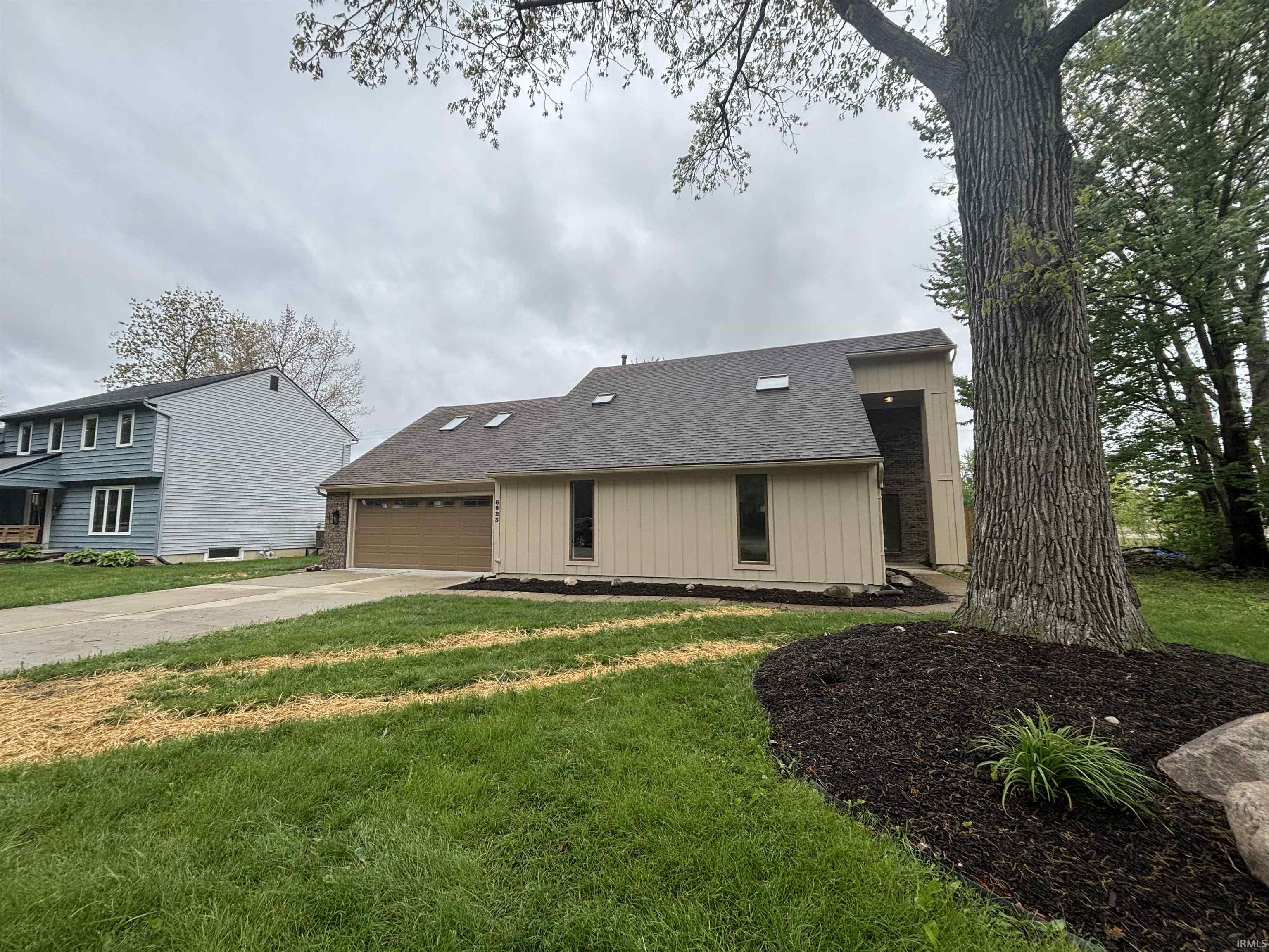 Contemporary residence featuring a two-car garage with a panel door, a prominent front entrance, and a light-colored exterior siding
