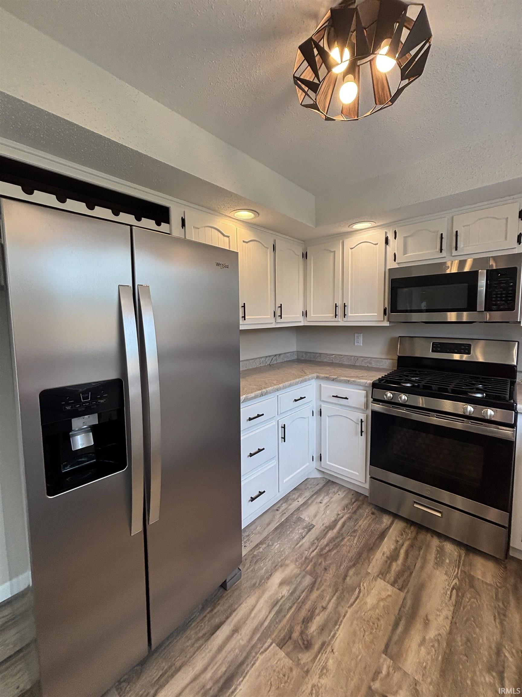Kitchen featuring white cabinetry, light countertops, wood-finish flooring, and stainless steel appliances including a side-by-side refrigerator, gas range, and microwave