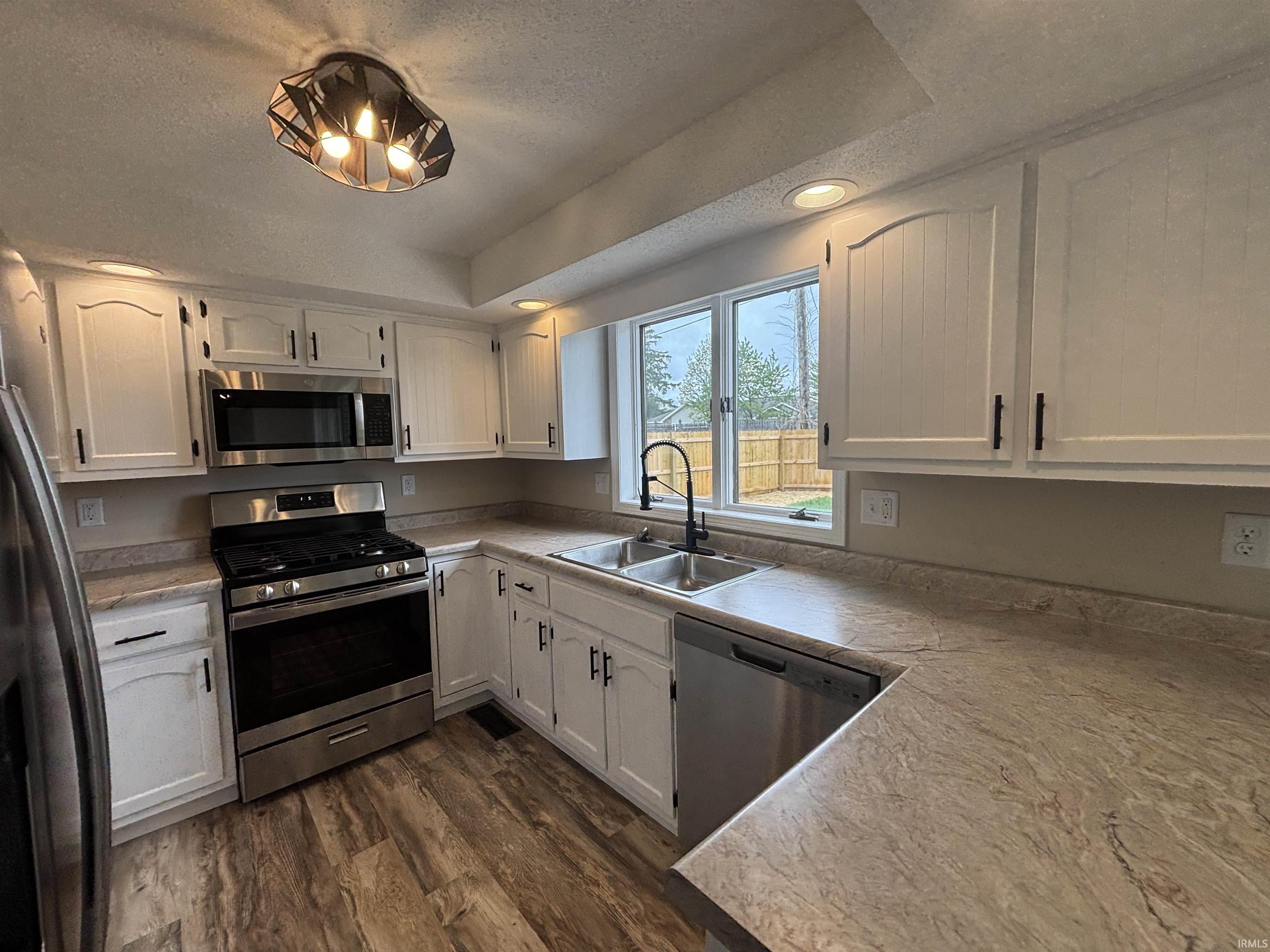 Updated kitchen featuring white cabinetry with dark hardware, stainless steel appliances, wood-finish flooring, and ample countertop space