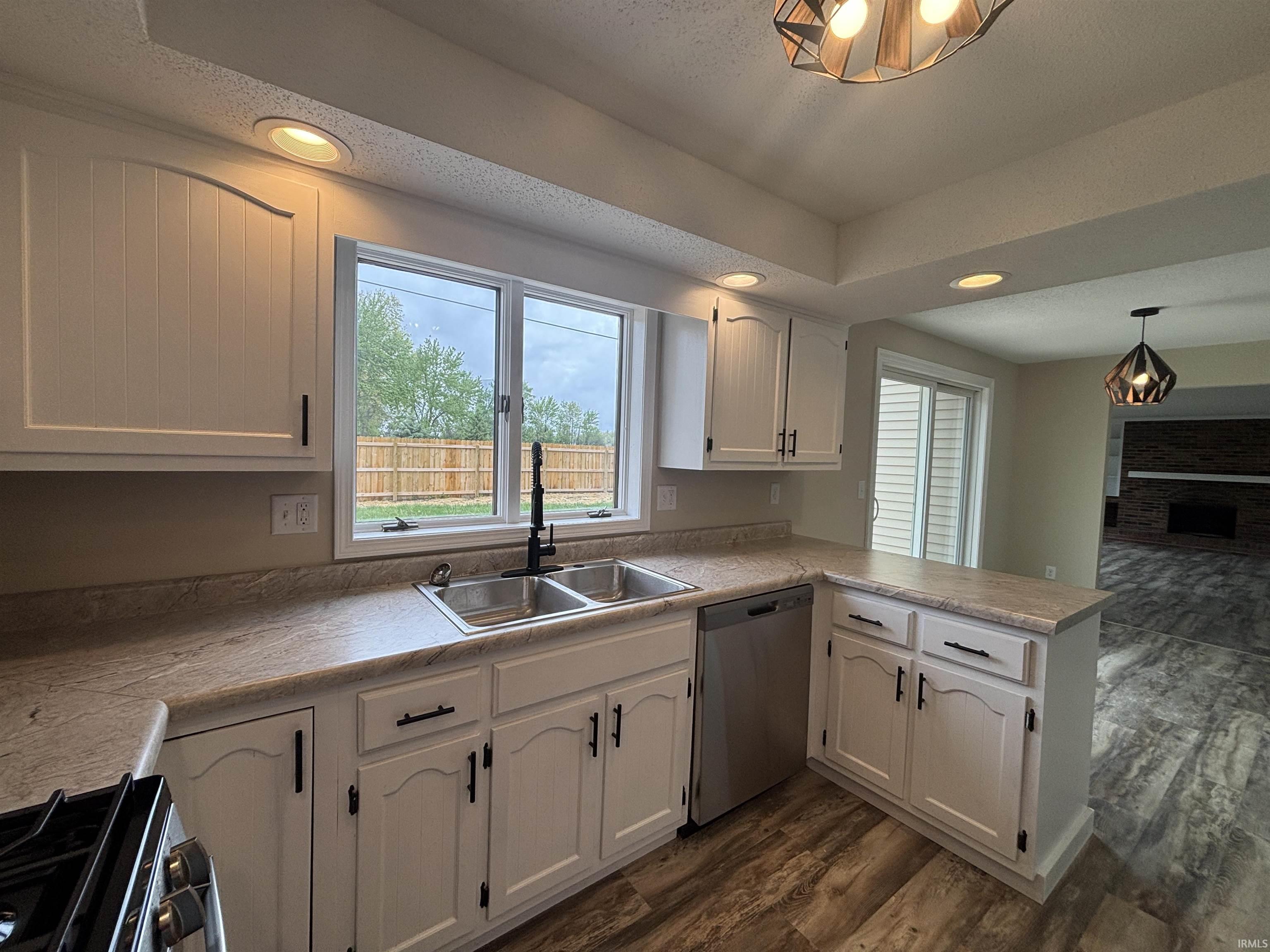 White cabinetry with matte black hardware, dual-basin stainless steel sink, stainless steel dishwasher, wood-finish flooring, and recessed lighting