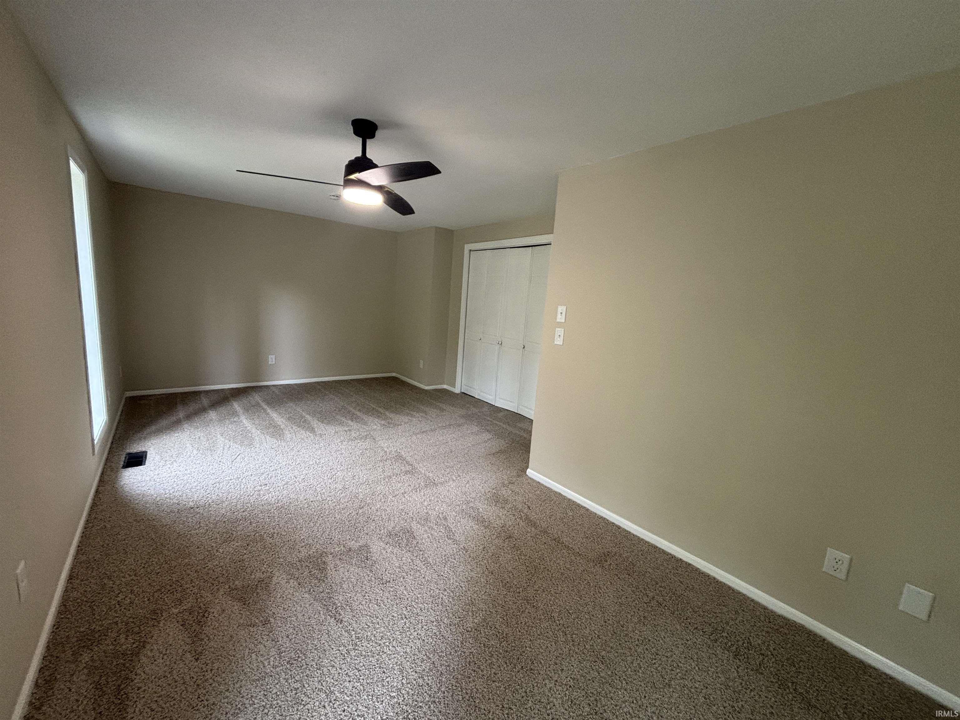Spacious room featuring neutral carpeting, light-toned walls, and a modern ceiling fan with integrated lighting