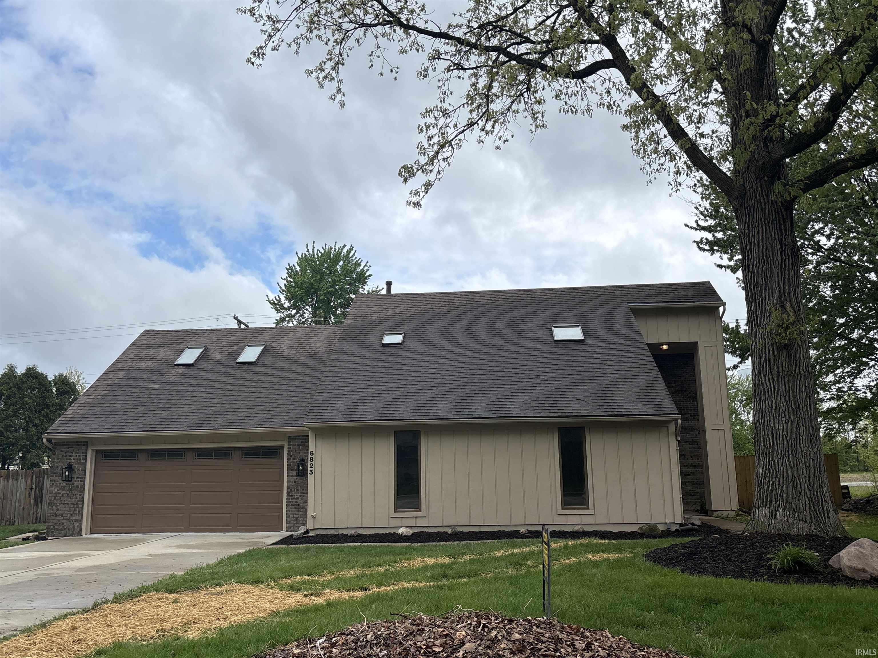 Split-level residence featuring a two-car garage with a brown door, stone accents on the facade, and multiple skylights
