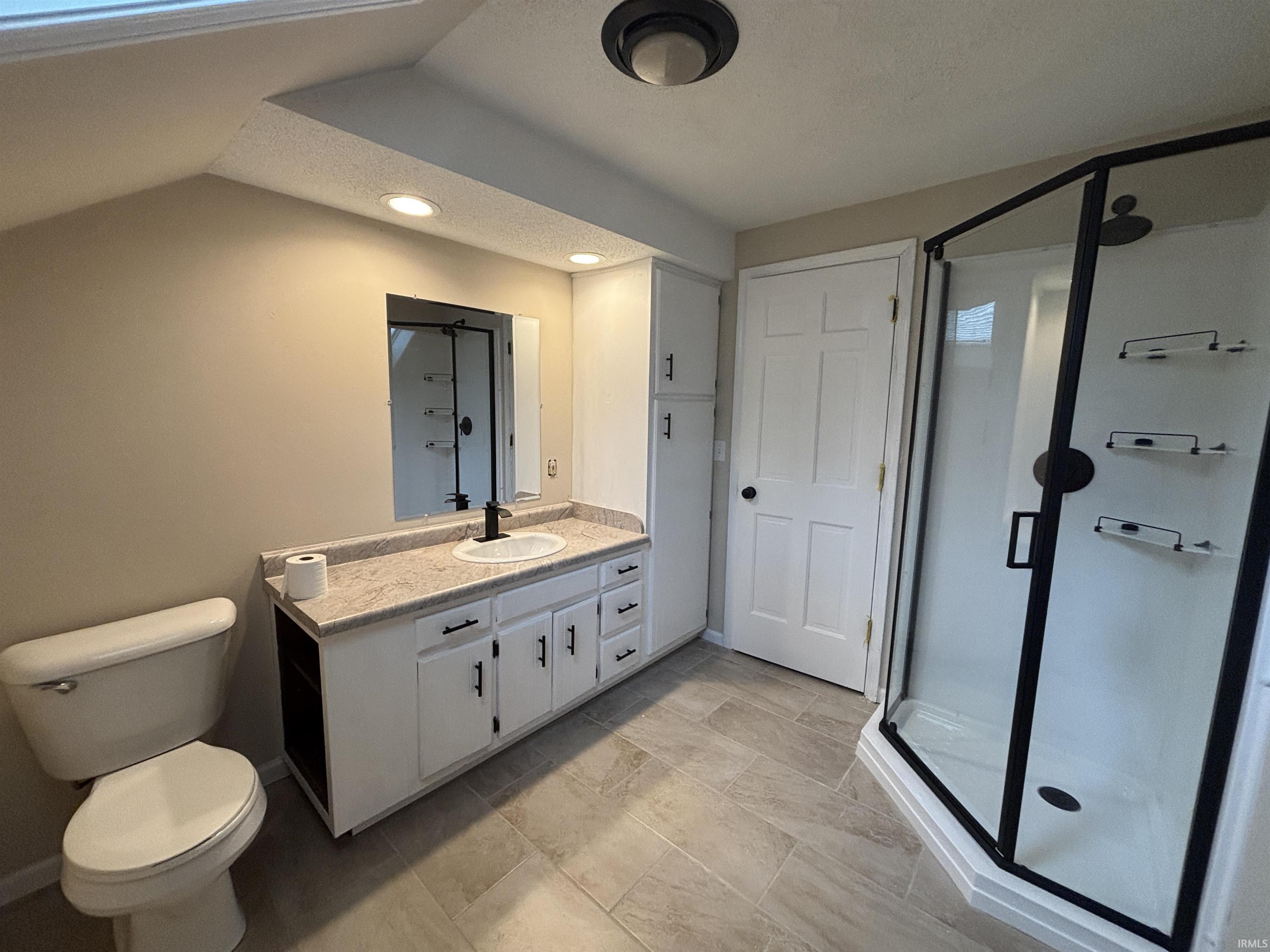 Full bathroom featuring a single vanity with storage, a corner shower with dark-framed glass enclosure, and light-toned tile flooring