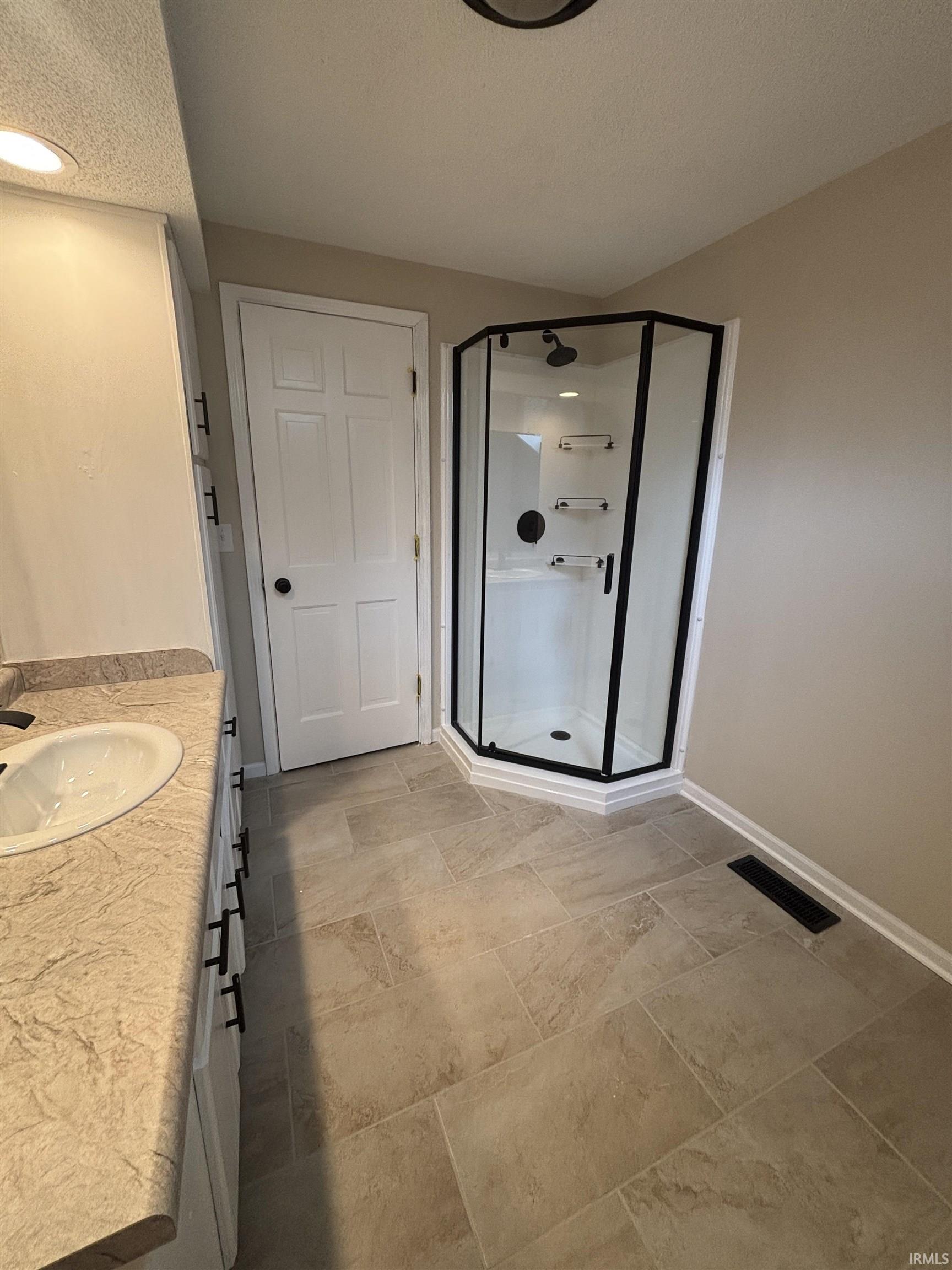 Bathroom featuring a corner shower with dark-framed glass enclosure, white vanity with integrated sink, patterned countertop, and light-toned tile flooring