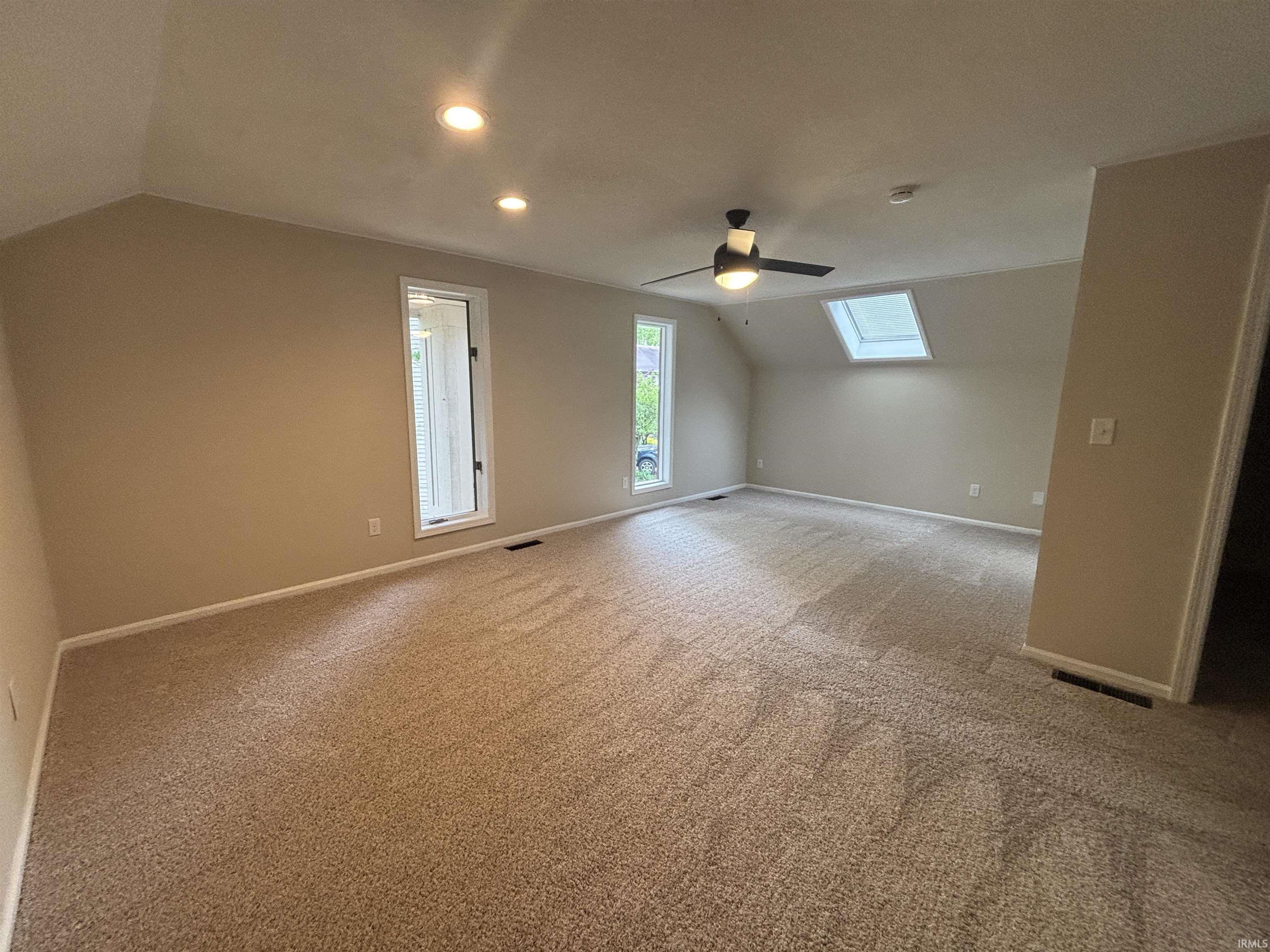 Spacious room featuring neutral carpet flooring, recessed lighting, two windows, a ceiling fan with integrated lighting, and a skylight
