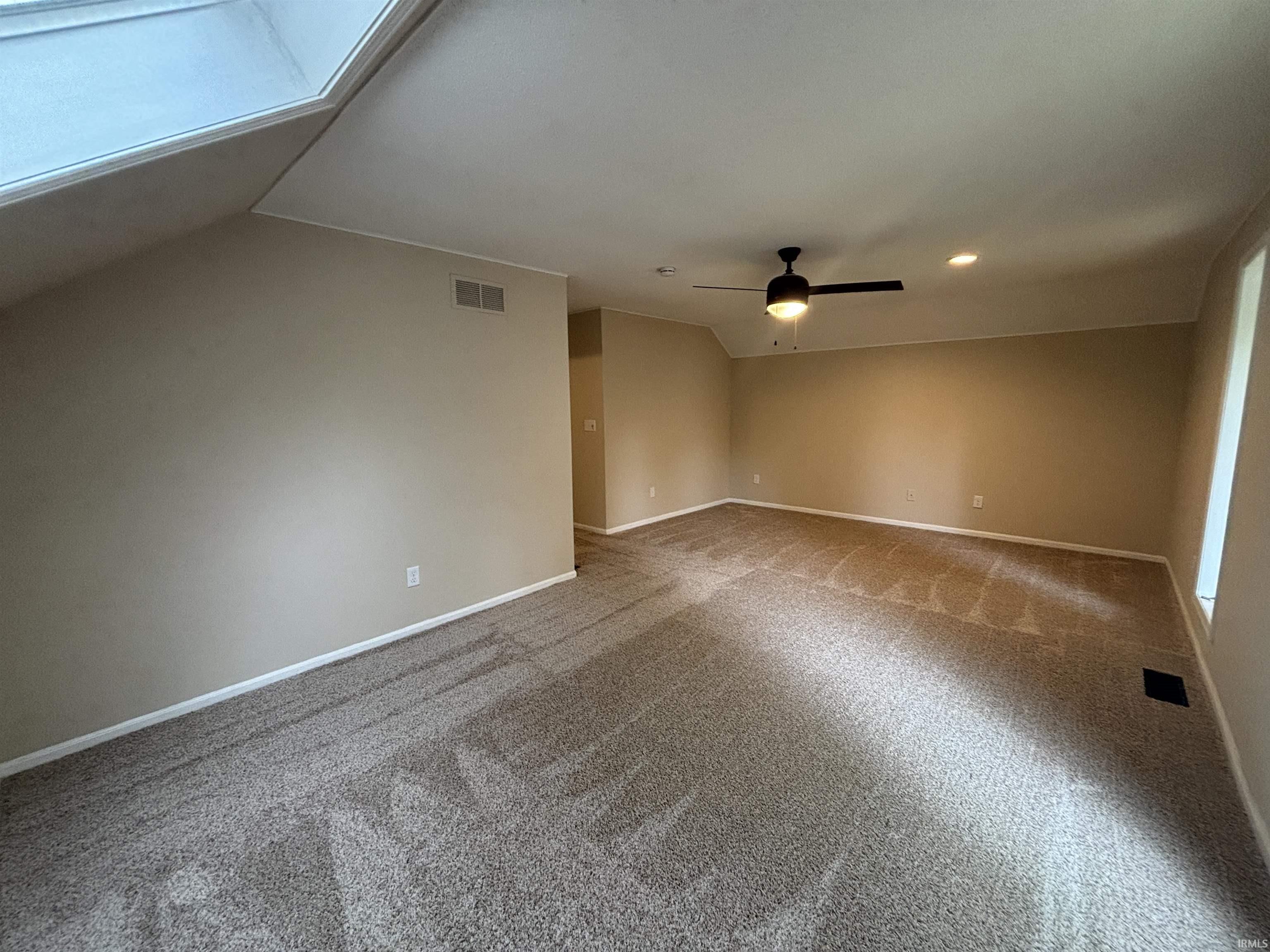 Spacious carpeted room featuring a skylight, ceiling fan with integrated lighting, recessed lighting, and baseboard molding