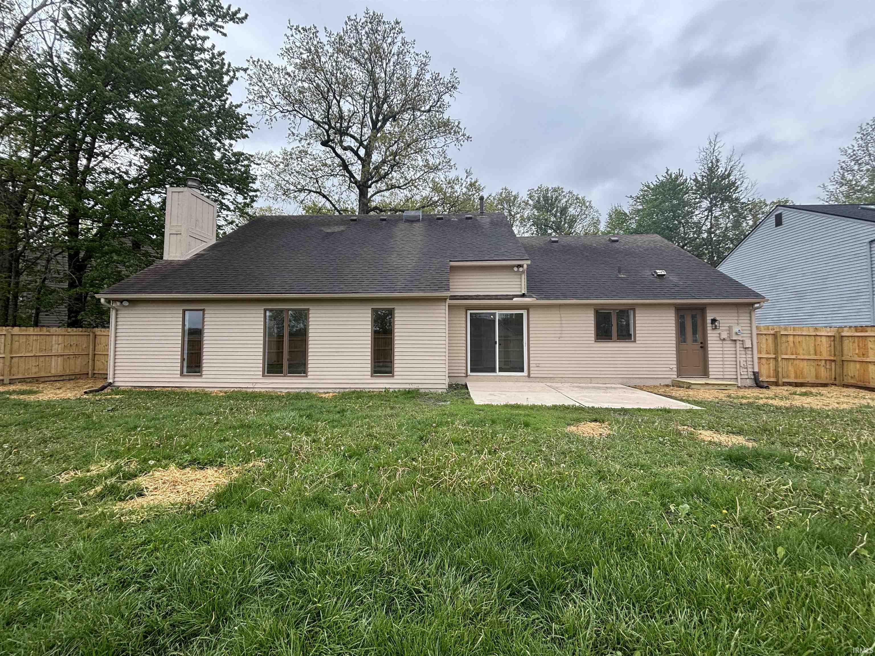 Expansive backyard featuring a new wood privacy fence, concrete patio, tan siding, and a prominent chimney