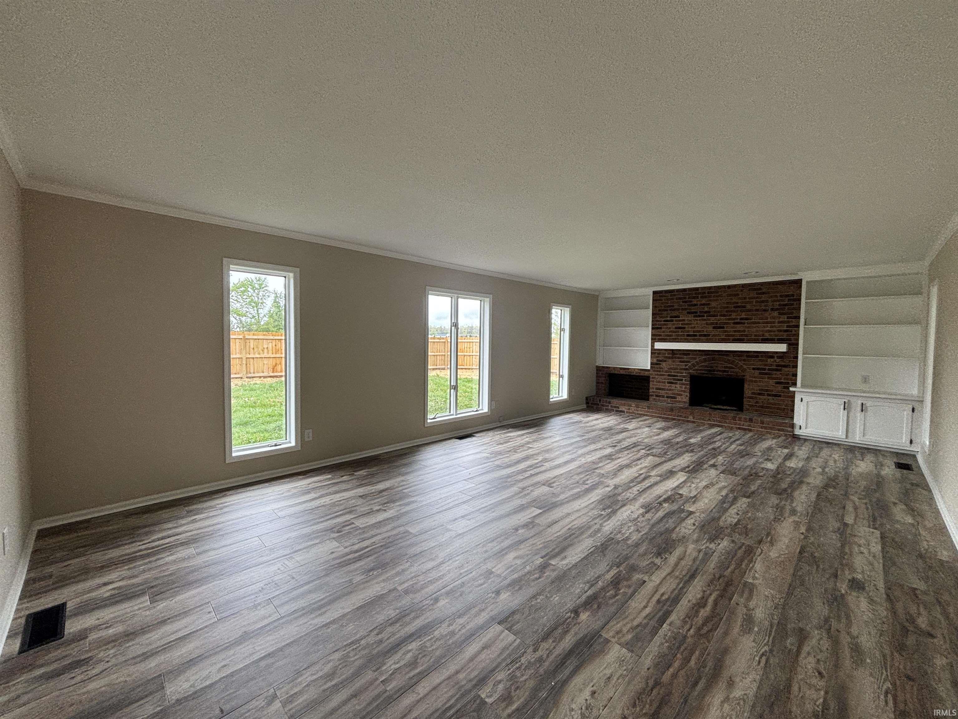 Spacious room featuring wood-finish flooring, a brick fireplace with mantel, built-in shelving, built-in cabinetry, and multiple windows