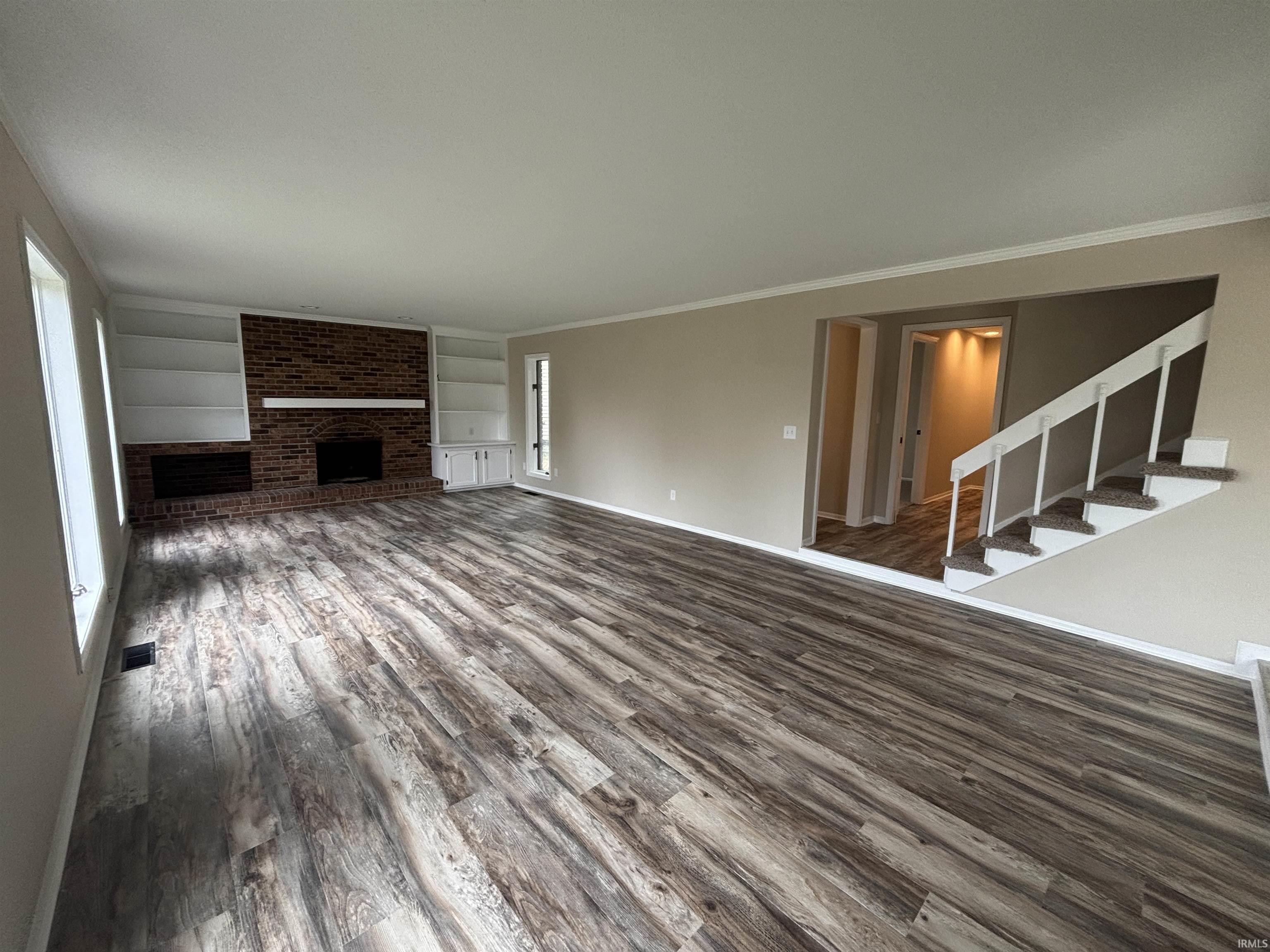 Spacious living area featuring wood-finish flooring, a brick fireplace with hearth, and built-in white shelving