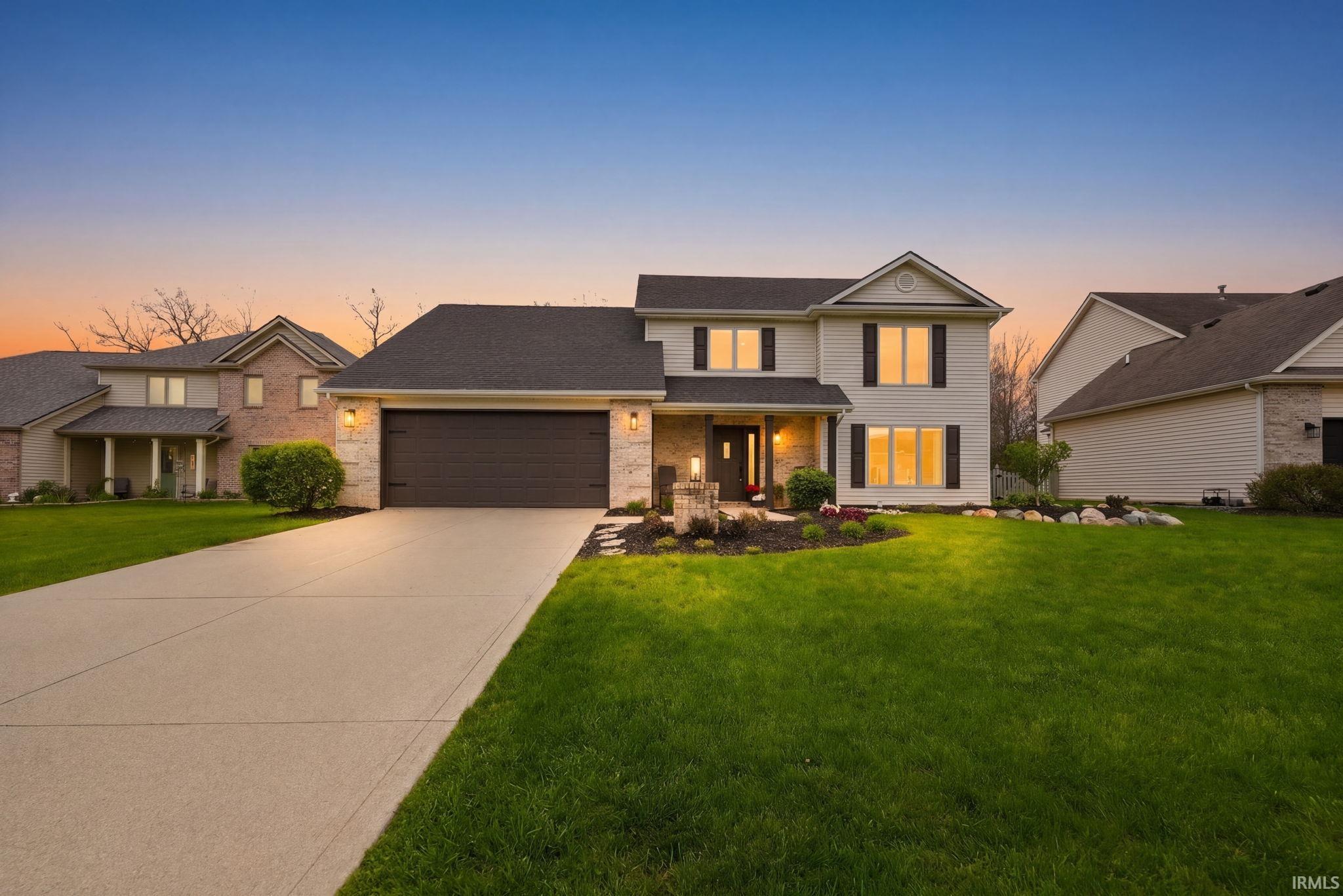 Two-story residence featuring a broad driveway, stone and siding exterior, front landscaping, and a two-car garage