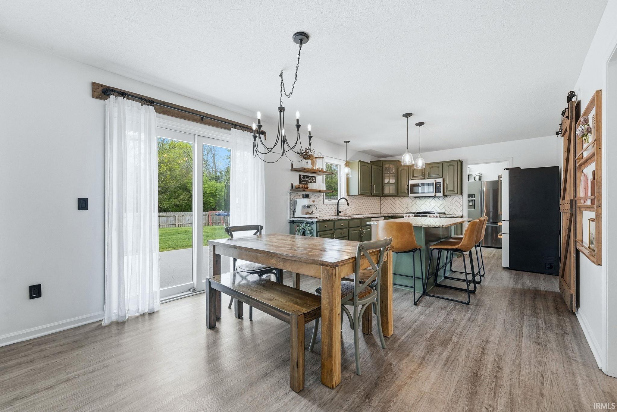 Open concept living space featuring wood-finish flooring, a kitchen with olive green cabinetry, a central island with a light-colored countertop and pendant lighting, and a dining area with a chandelier