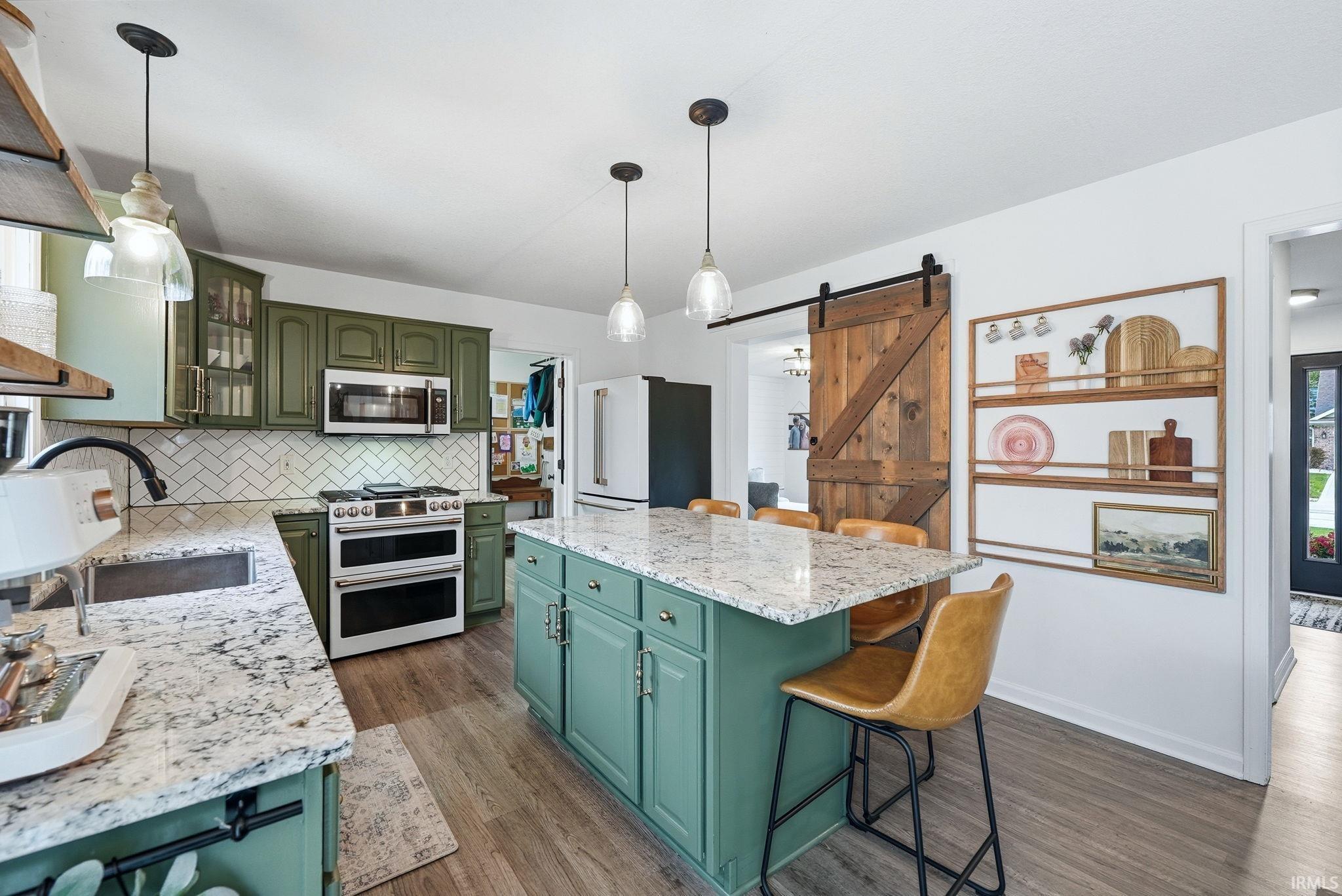 Kitchen featuring green cabinetry, granite-style countertops, herringbone tile backsplash, stainless steel appliances, and a central island with pendant lighting