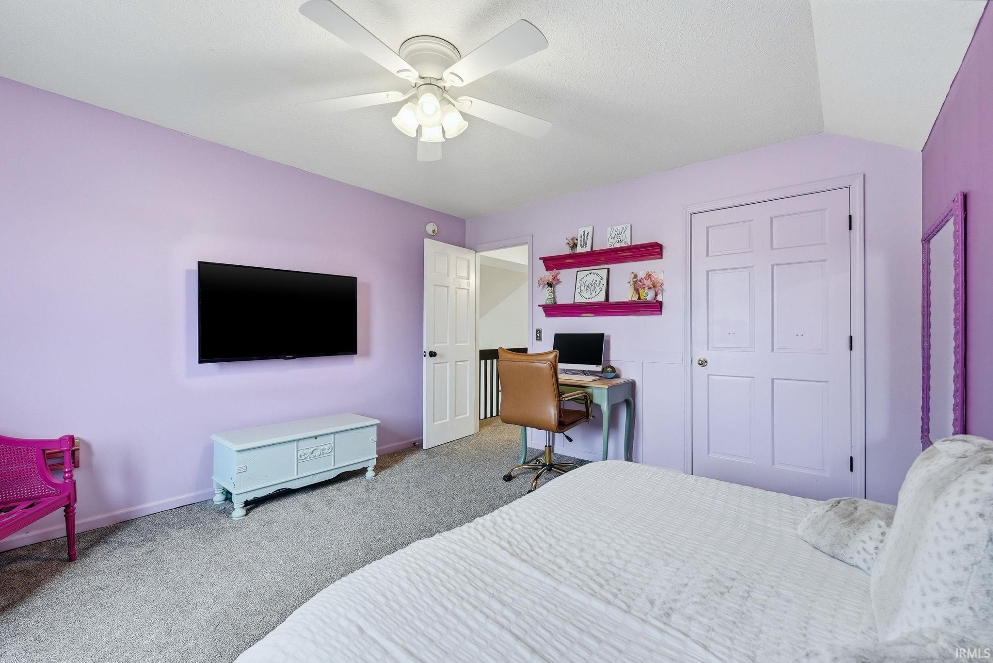 Carpeted room featuring a ceiling fan, wall-mounted television, and a built-in desk area with shelving