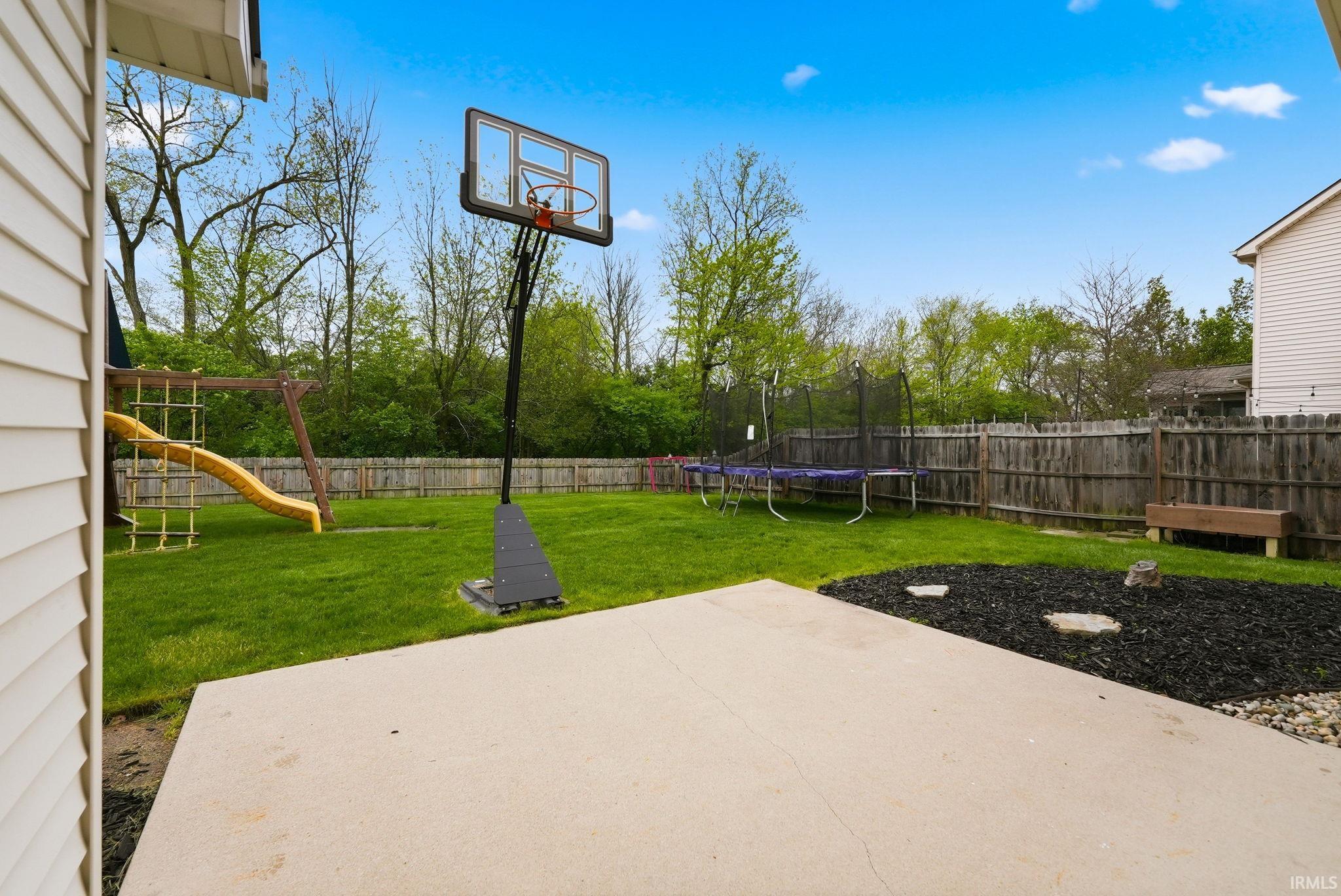 Expansive backyard featuring a concrete patio, lush green lawn, and a perimeter wood fence