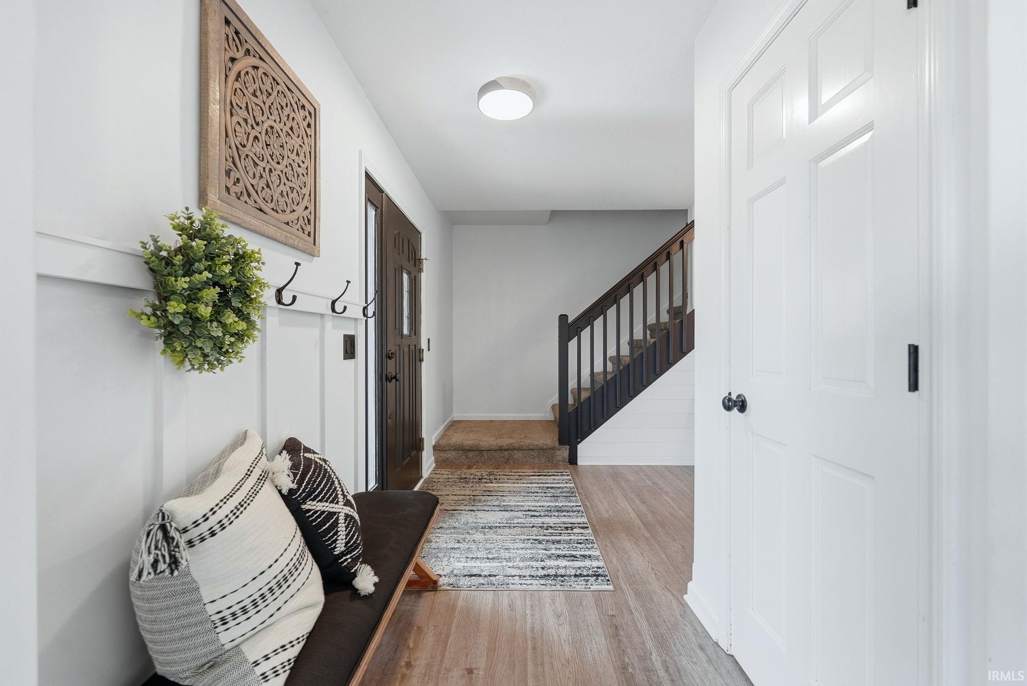 Entryway featuring wood-finish flooring, white paneled walls, a dark wood entry door, and a staircase with dark wood railings