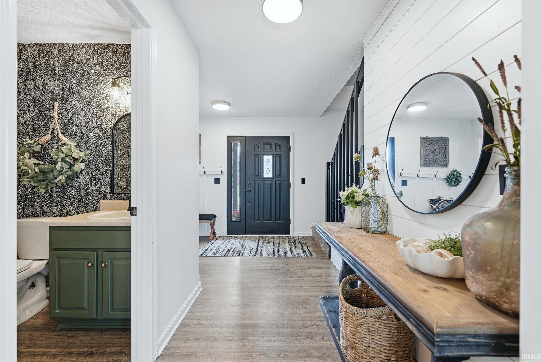 Welcoming entryway featuring wood-finish flooring, a solid black entry door with decorative glass inserts, and shiplap accent wall