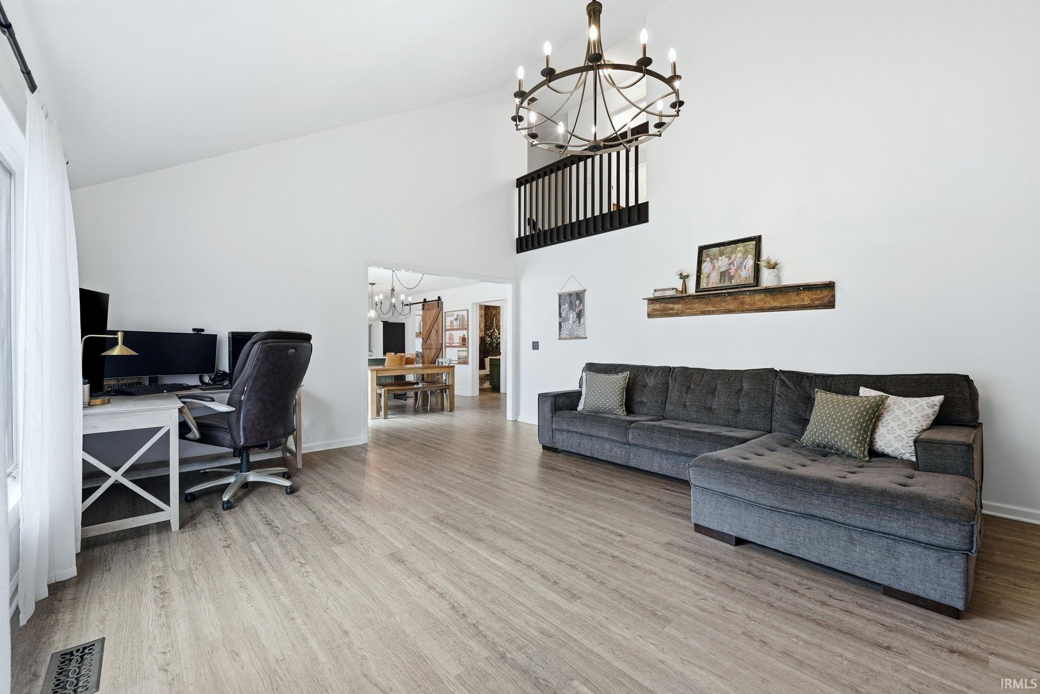 Vaulted ceiling with an overhead chandelier, wood-finish flooring throughout, and a balcony with black balusters