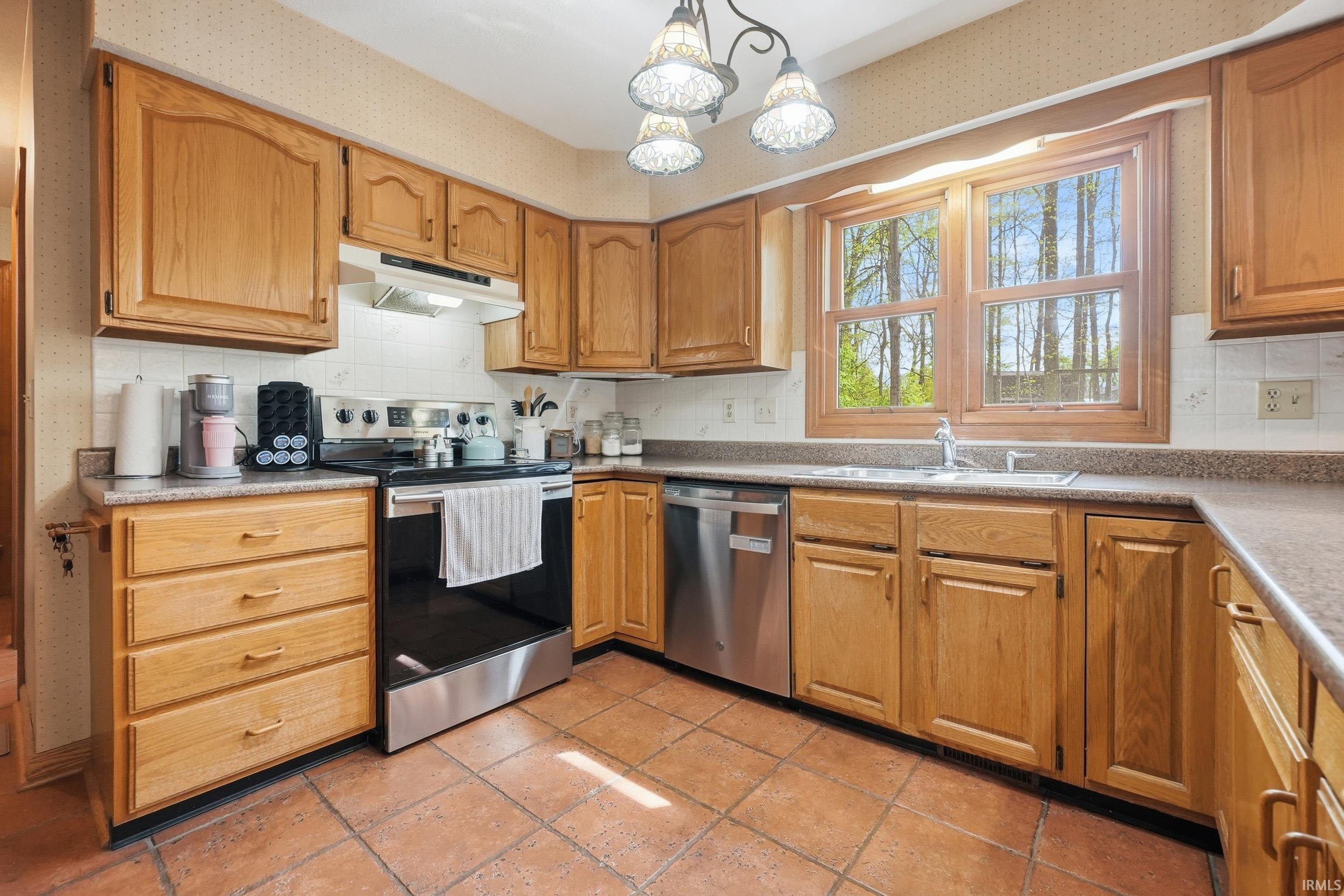 Kitchen featuring wood-finish cabinetry, tile flooring, stainless steel appliances, and a window above the sink