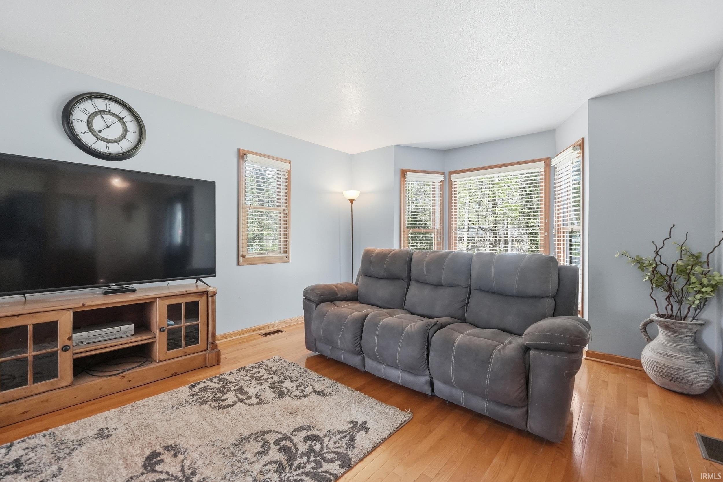 Living space featuring wood-finish flooring, light blue wall paint, and multiple windows with wood-frame blinds