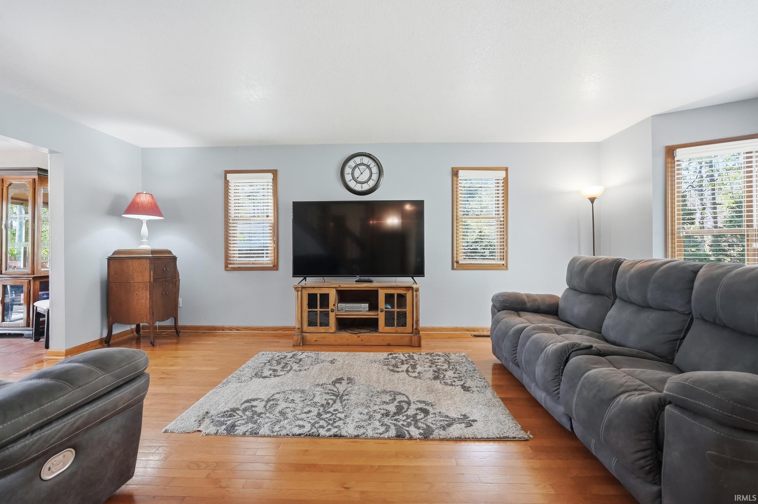 Living area featuring wood-finish flooring, light blue wall paint, and multiple windows with wood trim