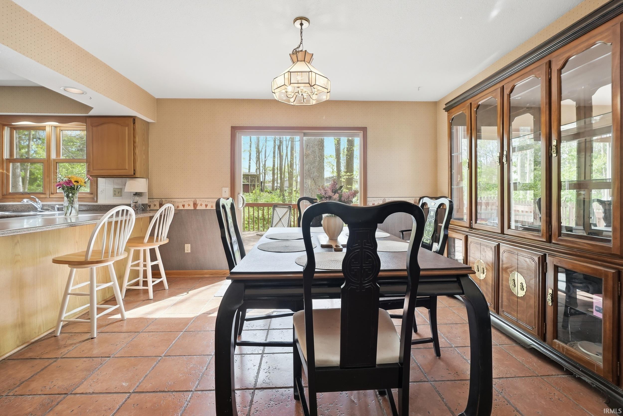 Open-concept dining area with terracotta-style tile flooring, featuring a large sliding glass door, a built-in display cabinet, and a breakfast bar with seating
