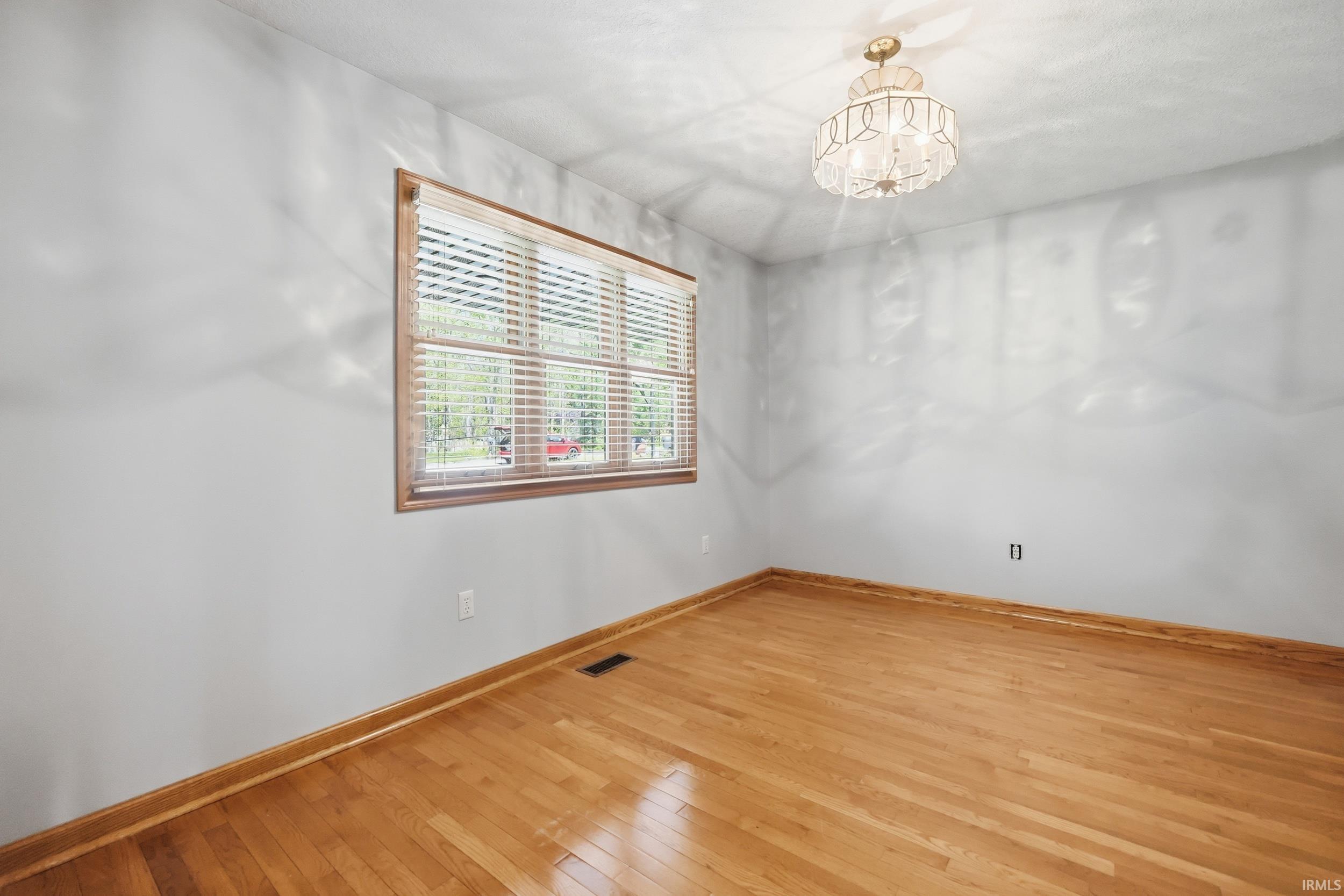 Room with wood-finish flooring, light grey walls, and a white popcorn ceiling