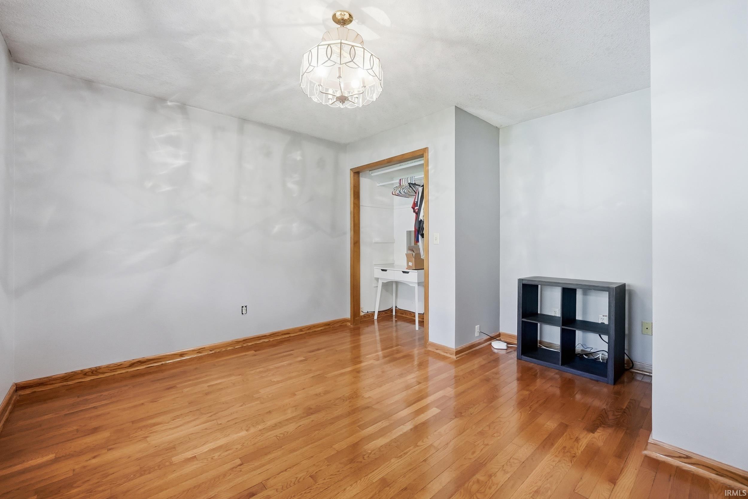 Room featuring wood-finish flooring, a decorative ceiling light fixture, and a closet with wood trim