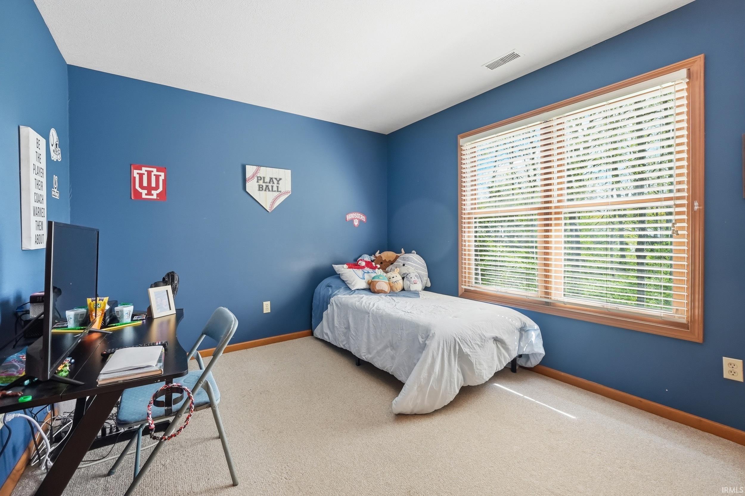 Light-filled room featuring a large window with natural wood trim, horizontal blinds, and cream-colored carpeting
