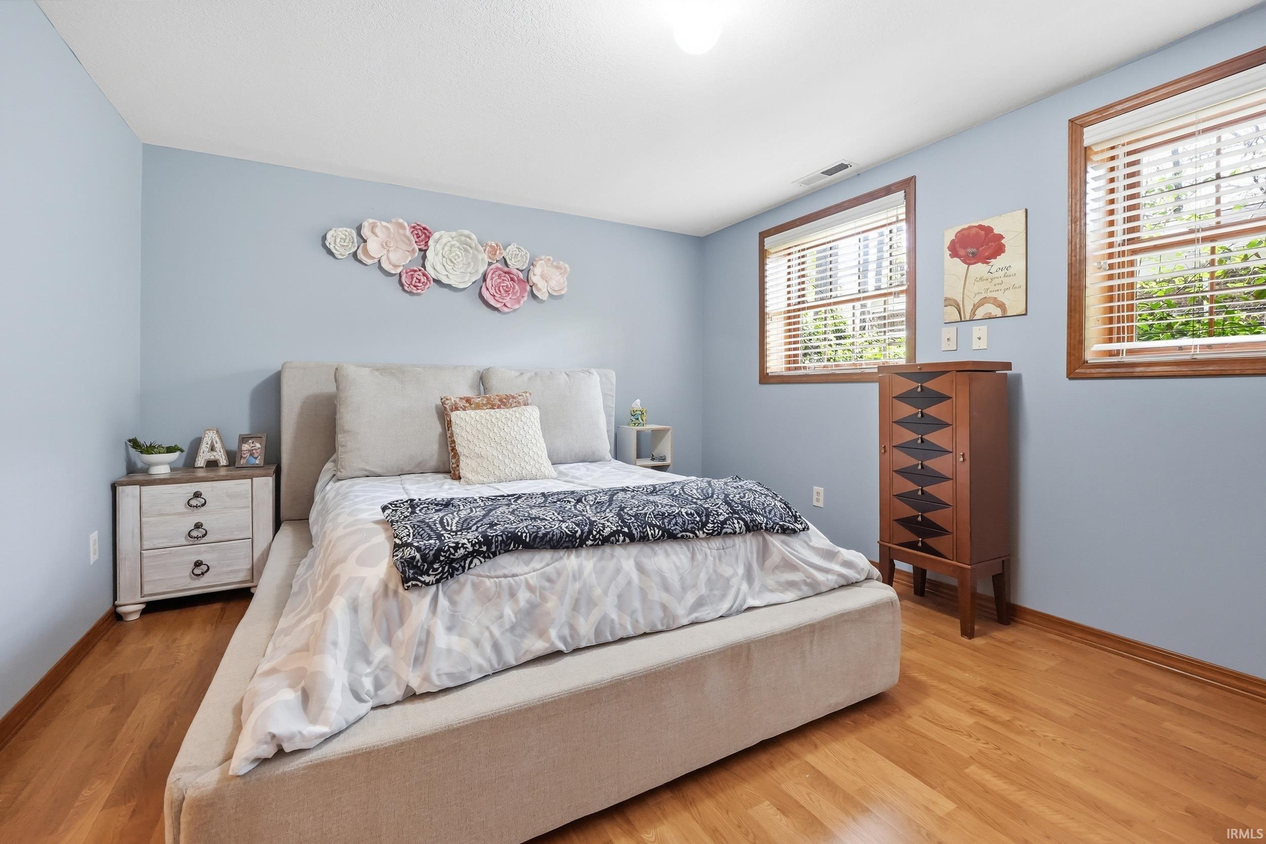 Interior room featuring wood-finish flooring, two large windows with horizontal blinds, and a built-in air vent