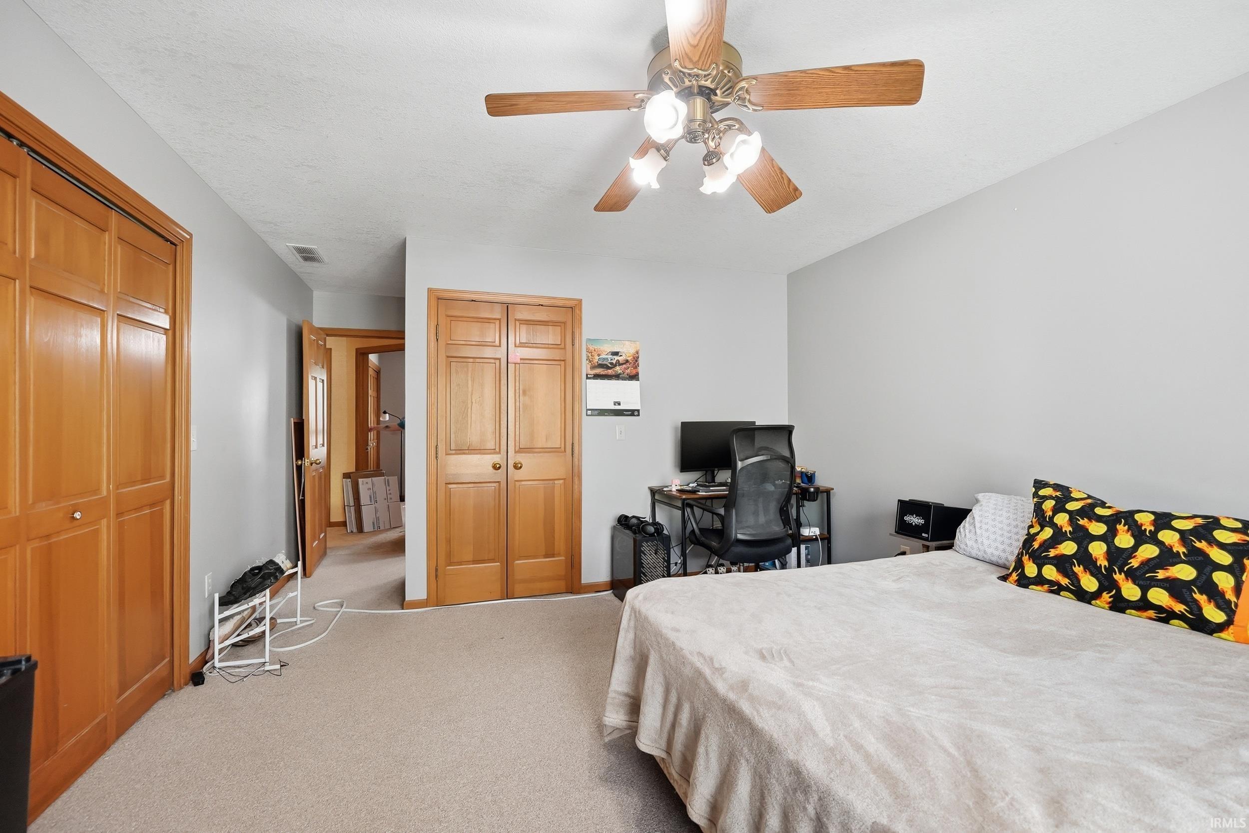 Carpeted room featuring light gray walls, a ceiling fan with light fixture, and two sets of bi-fold closet doors with wood-finish panels