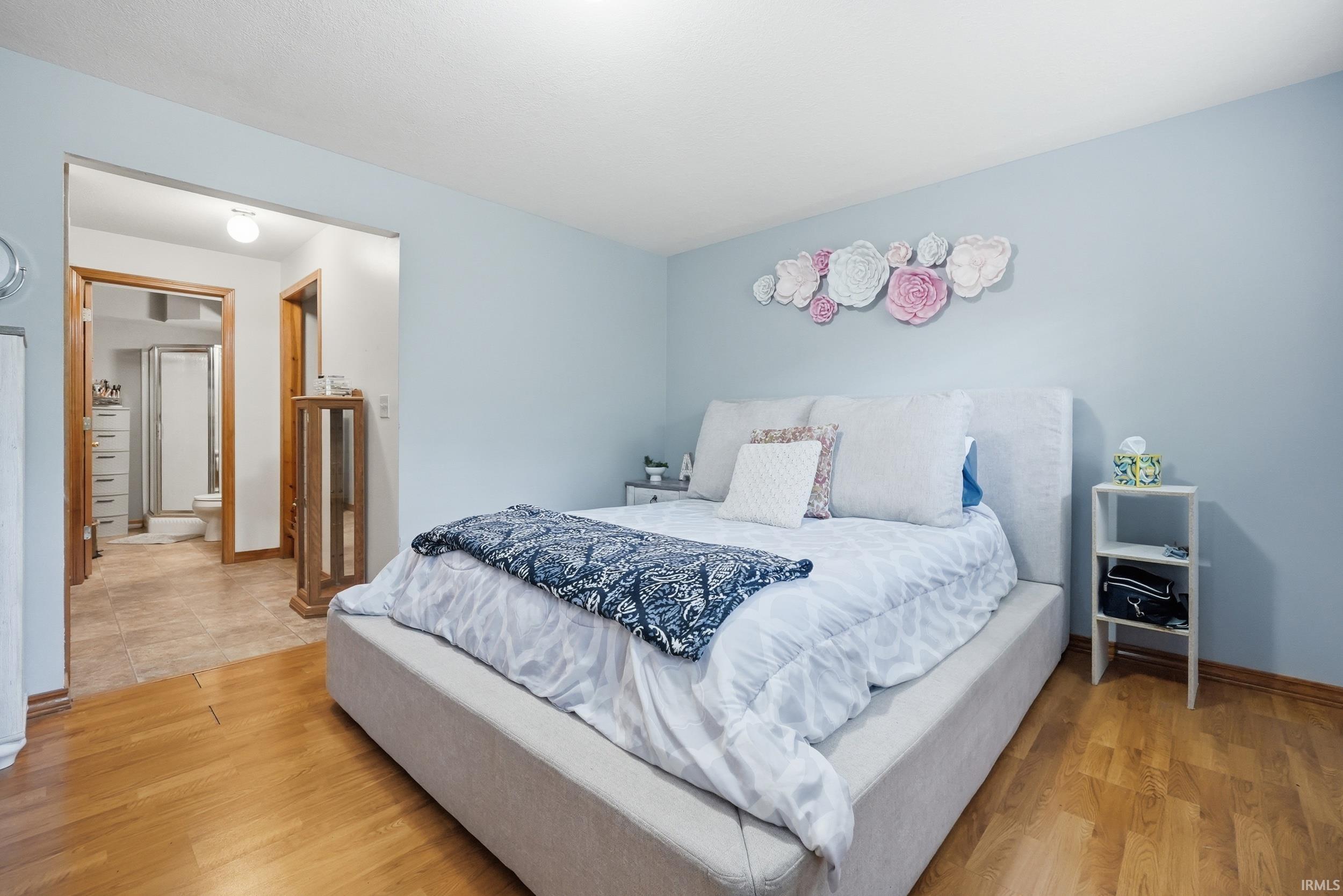 Wood-finish flooring extends throughout this room, featuring a doorway that opens to a tiled area with a shower enclosure