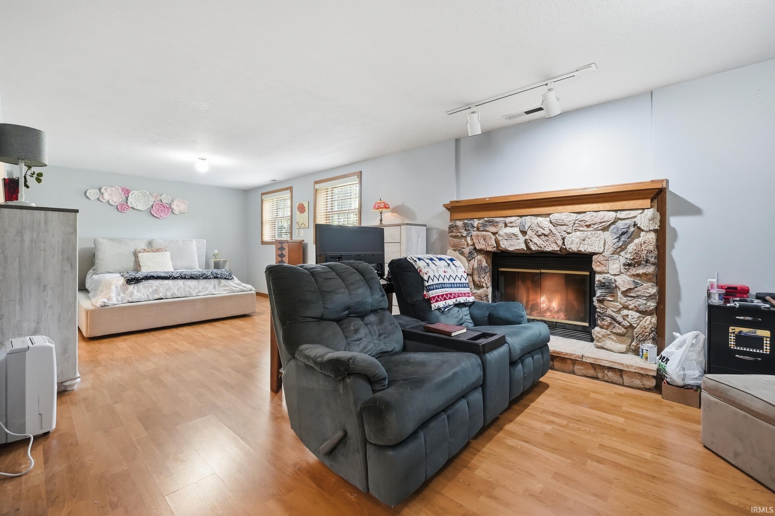 Spacious room featuring wood-finish flooring, a stone-faced fireplace with a wood mantel, and multiple windows