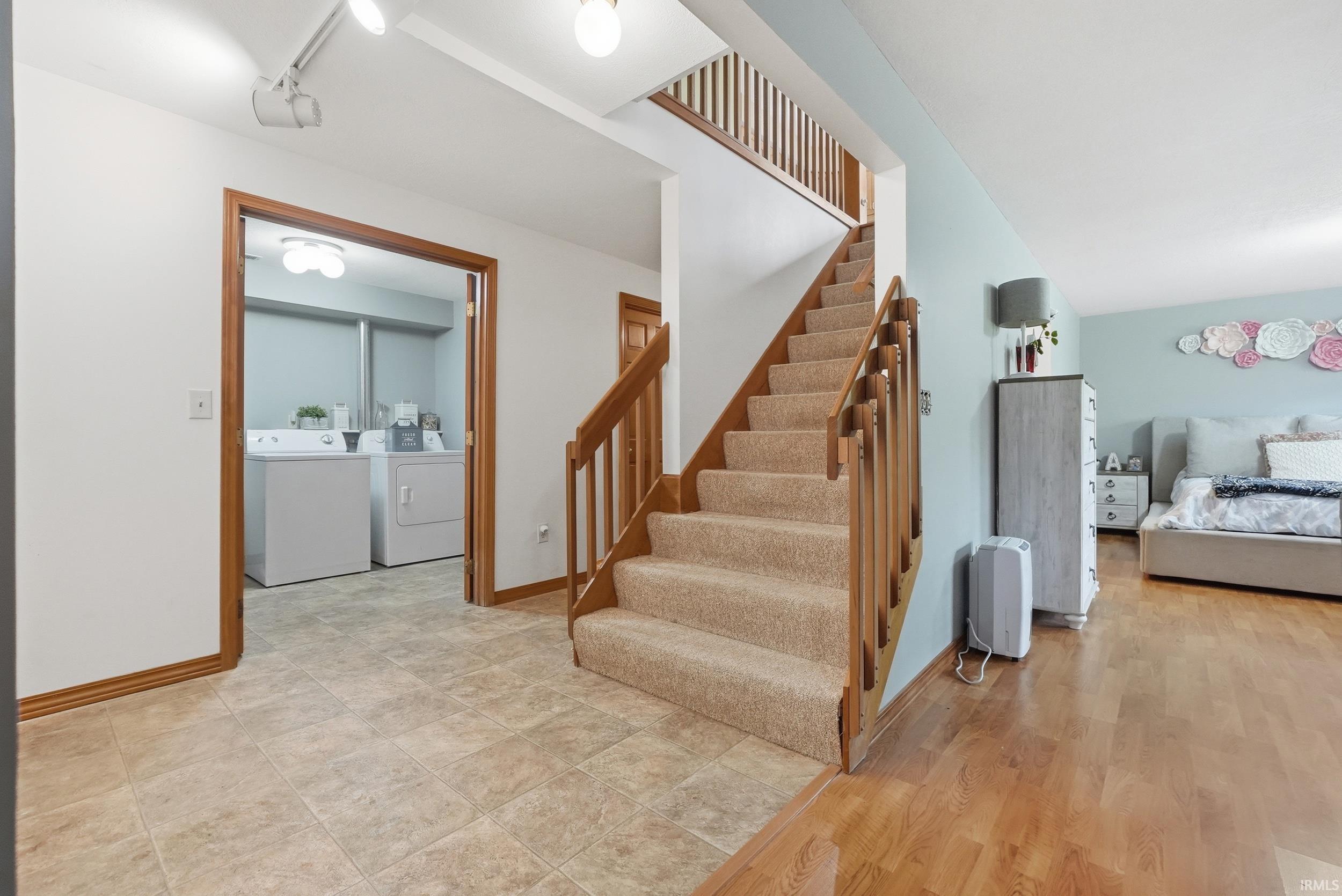 Carpeted staircase with wooden banister, tiled flooring, wood-finish flooring, and a dedicated laundry area with washer and dryer hookups