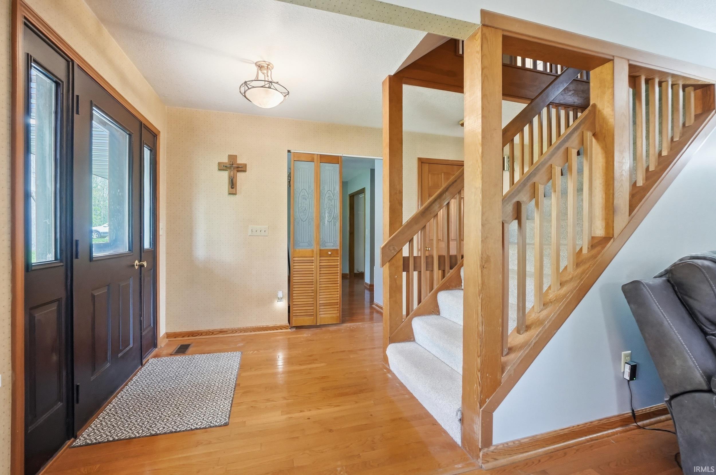 Foyer featuring a dual-pane entry door with sidelights, wood-finish flooring, a contemporary flush-mount ceiling light, and a wooden staircase with carpeted treads