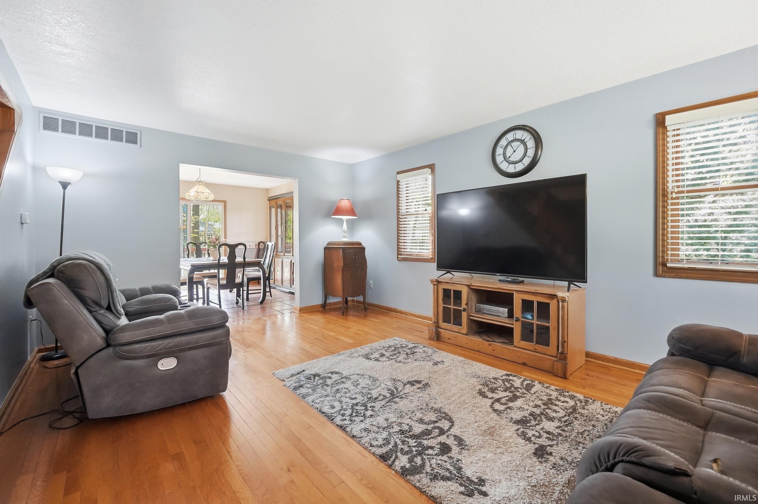 Living area featuring wood-finish flooring, light blue walls, and multiple windows with blinds
