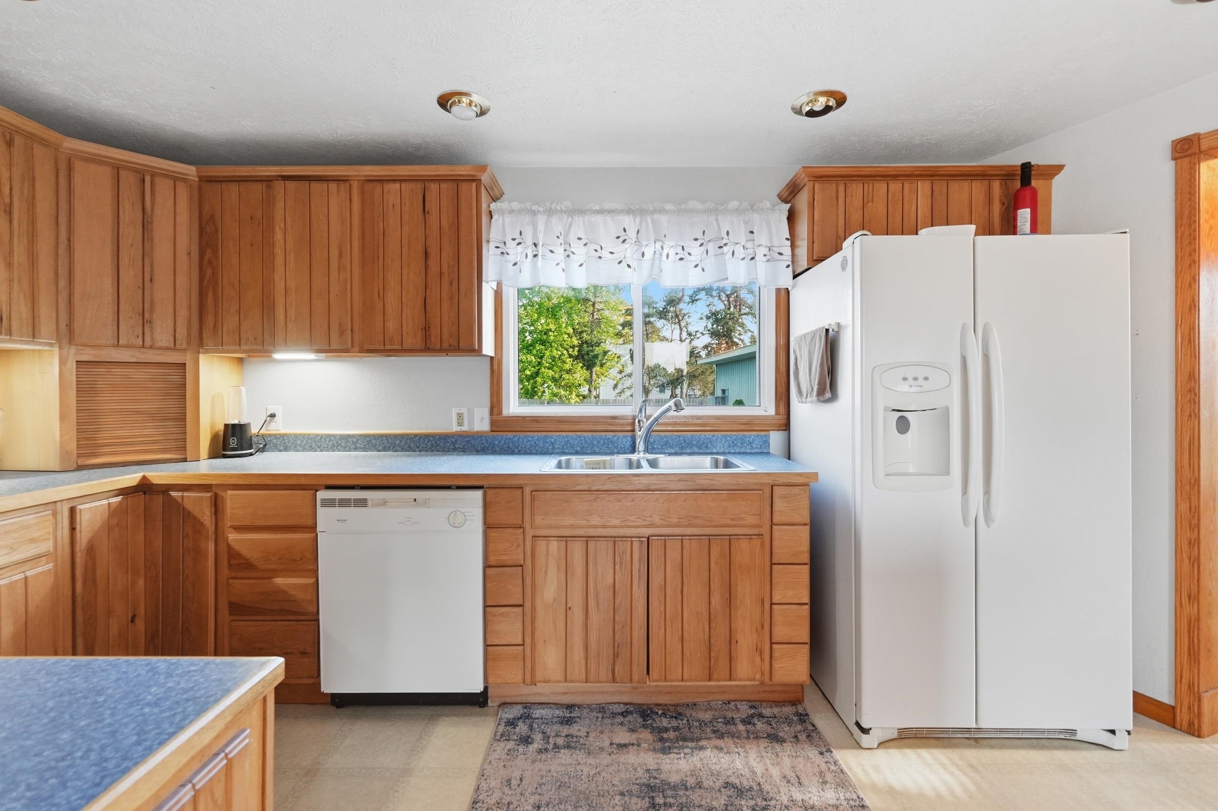 Kitchen featuring natural wood cabinetry, blue laminate countertops, a white side-by-side refrigerator, a stainless steel sink, and a white dishwasher
