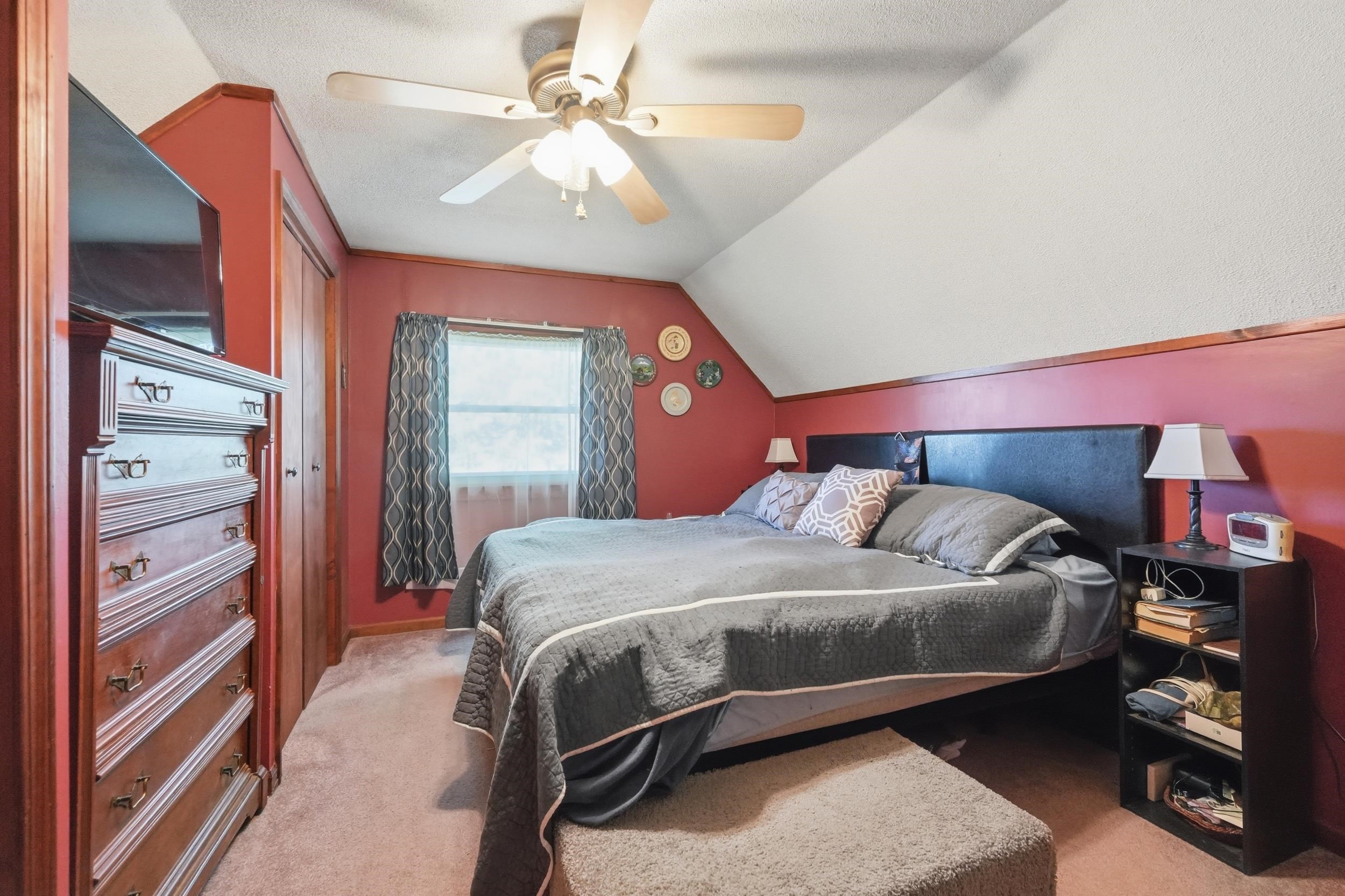 Carpeted room featuring sloped ceilings, a window with curtains, and a ceiling fan with integrated lighting