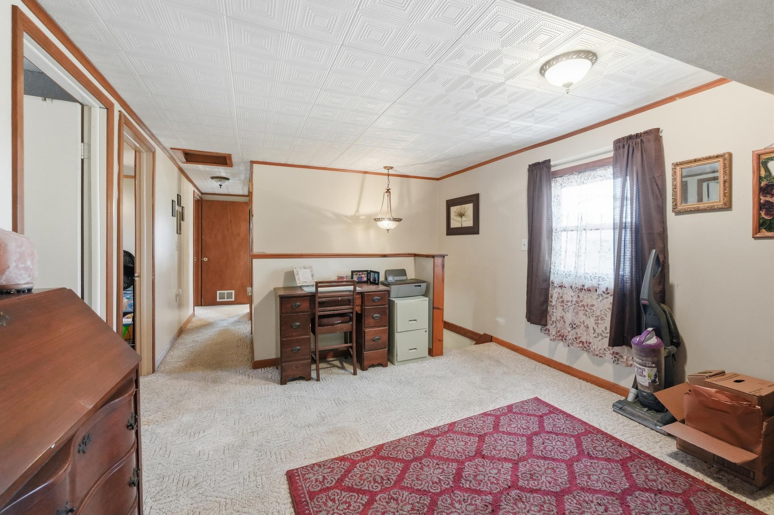 Carpeted room with white textured ceiling panels and neutral-toned walls featuring wood trim