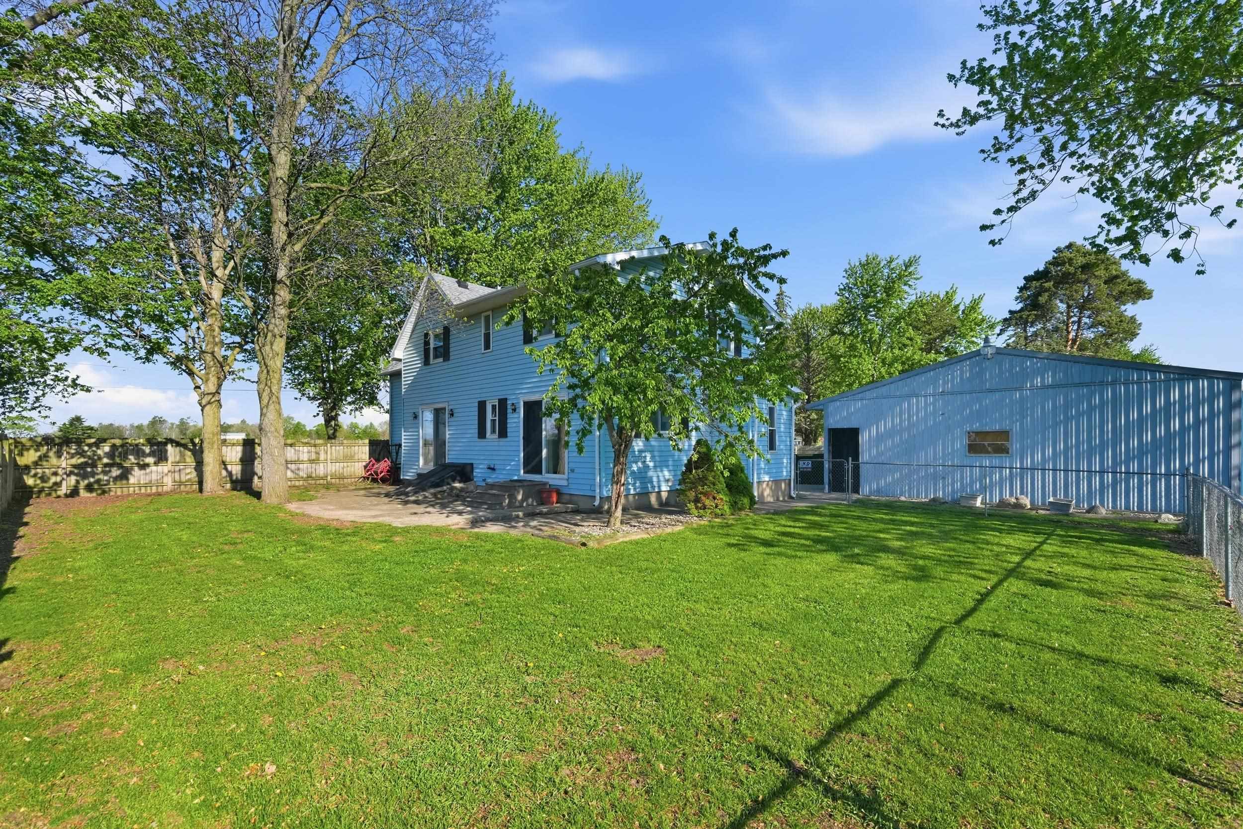 Expansive rear yard featuring a detached auxiliary building, mature trees, a concrete patio, and a chain-link fence