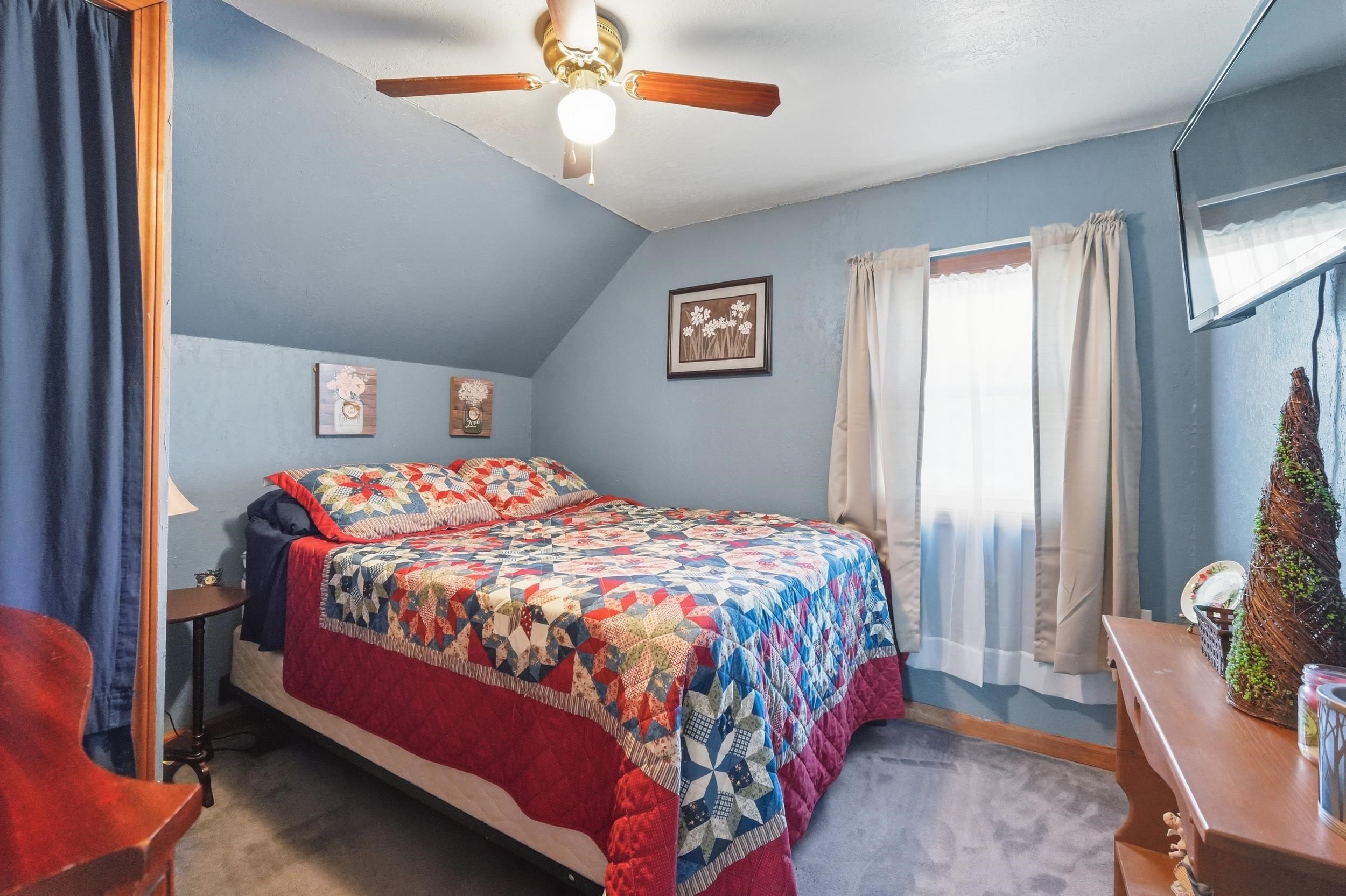 Bedroom featuring sloped ceilings, a ceiling fan with integrated lighting, window with drapes, and carpeting