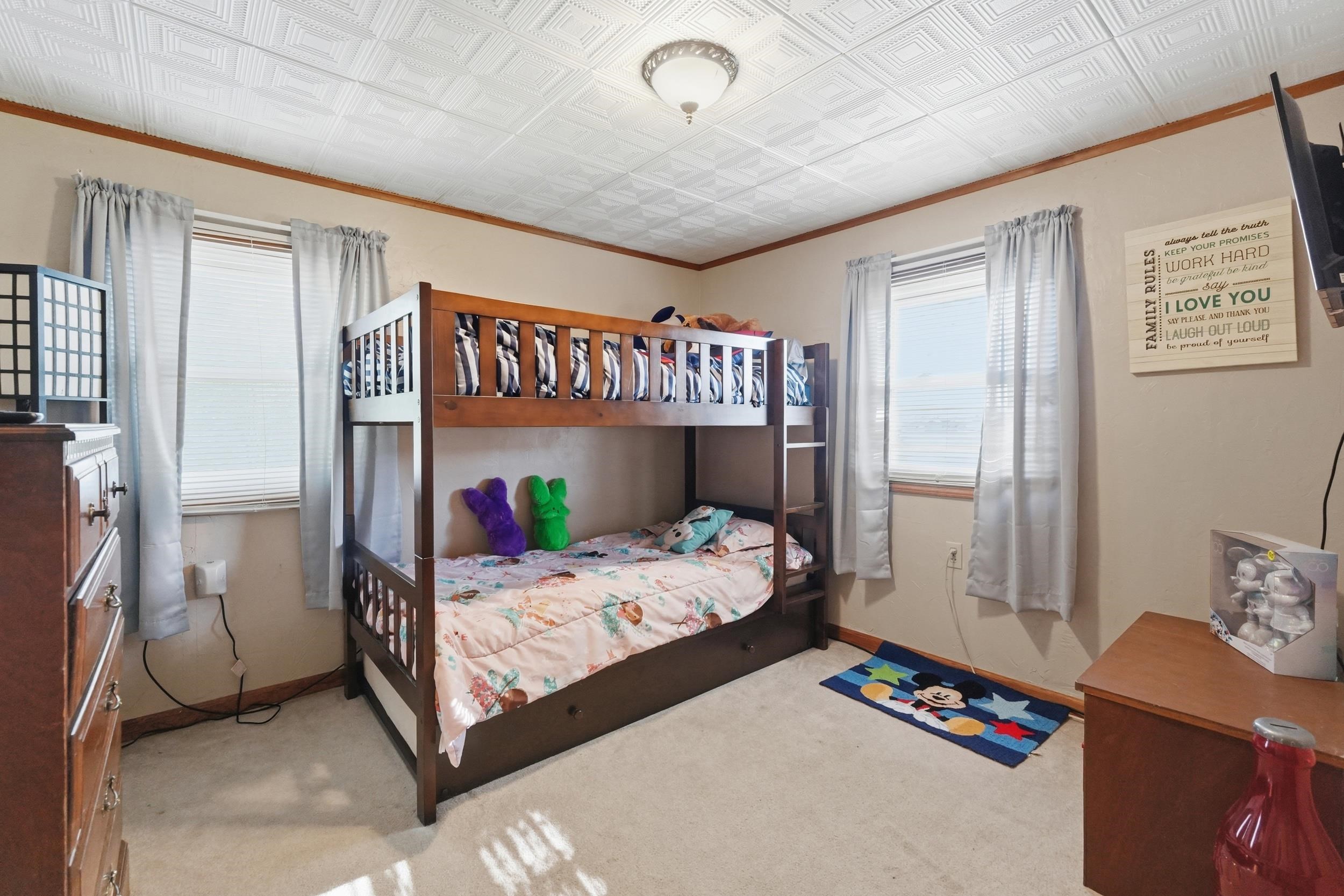 Room featuring carpeted flooring, two windows with blinds and curtains, a ceiling light fixture, and a textured ceiling