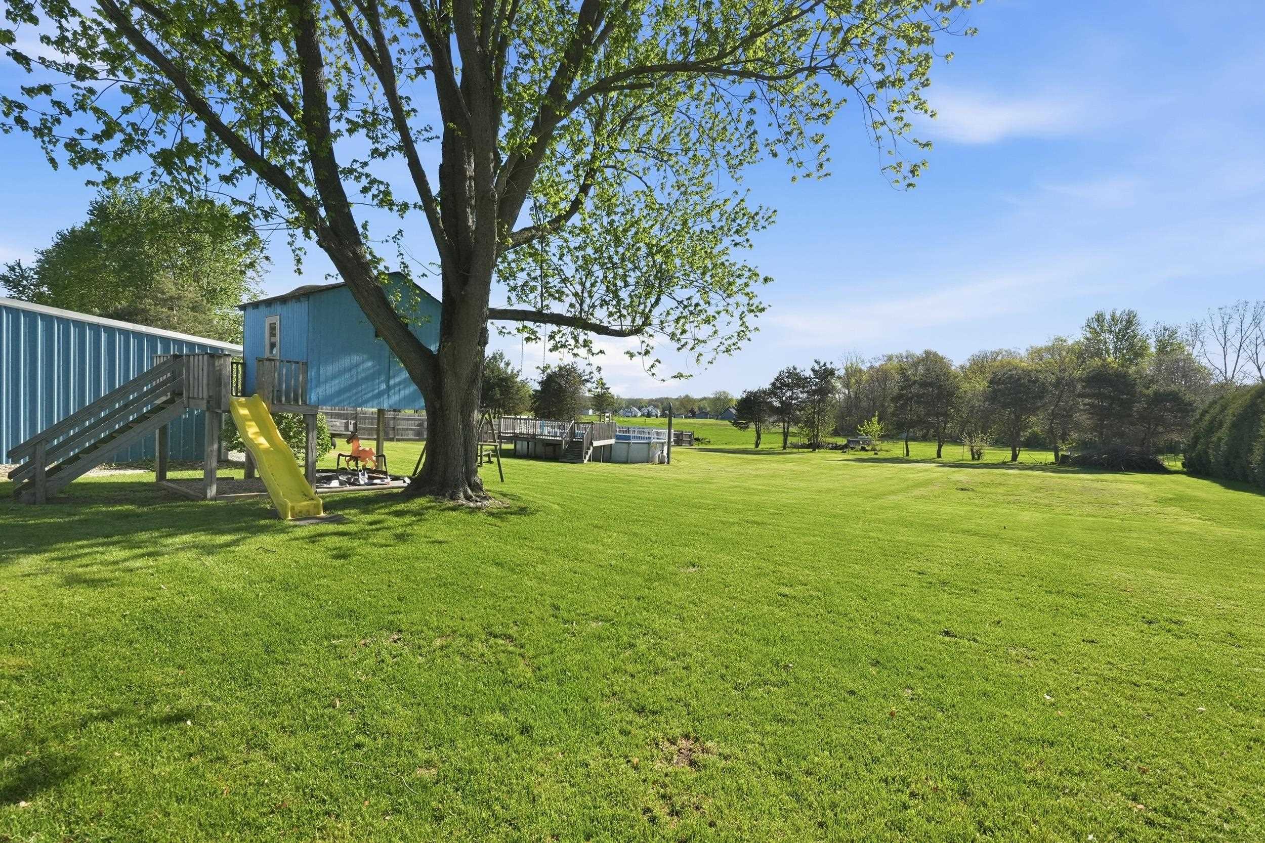 Expansive green lawn with mature trees and a dedicated recreational area featuring a play structure