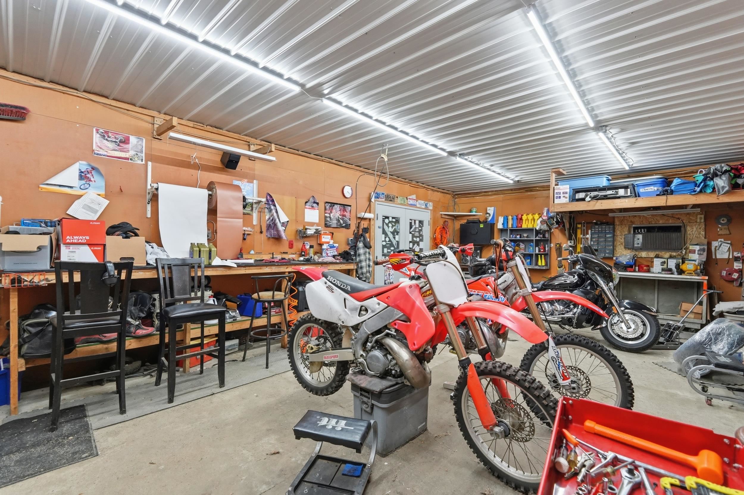 Spacious garage with corrugated metal ceiling, ample overhead lighting, built-in workbench, and extensive shelving for storage
