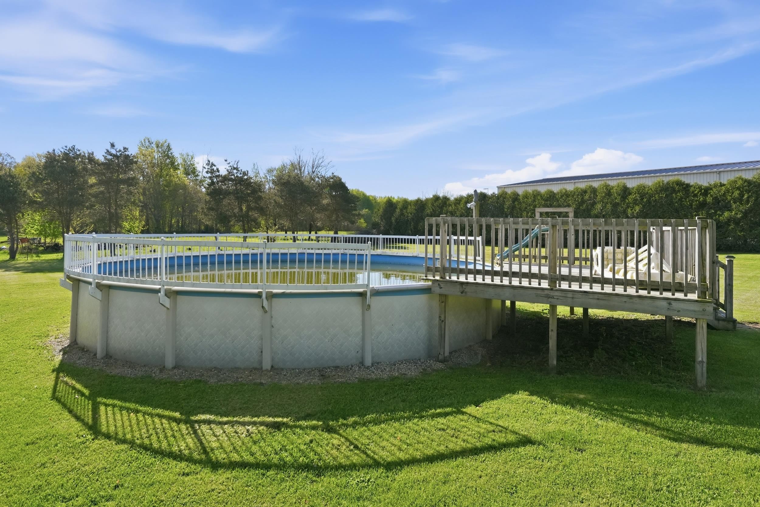 Expansive backyard featuring an above-ground pool with a surrounding wooden deck and safety railing
