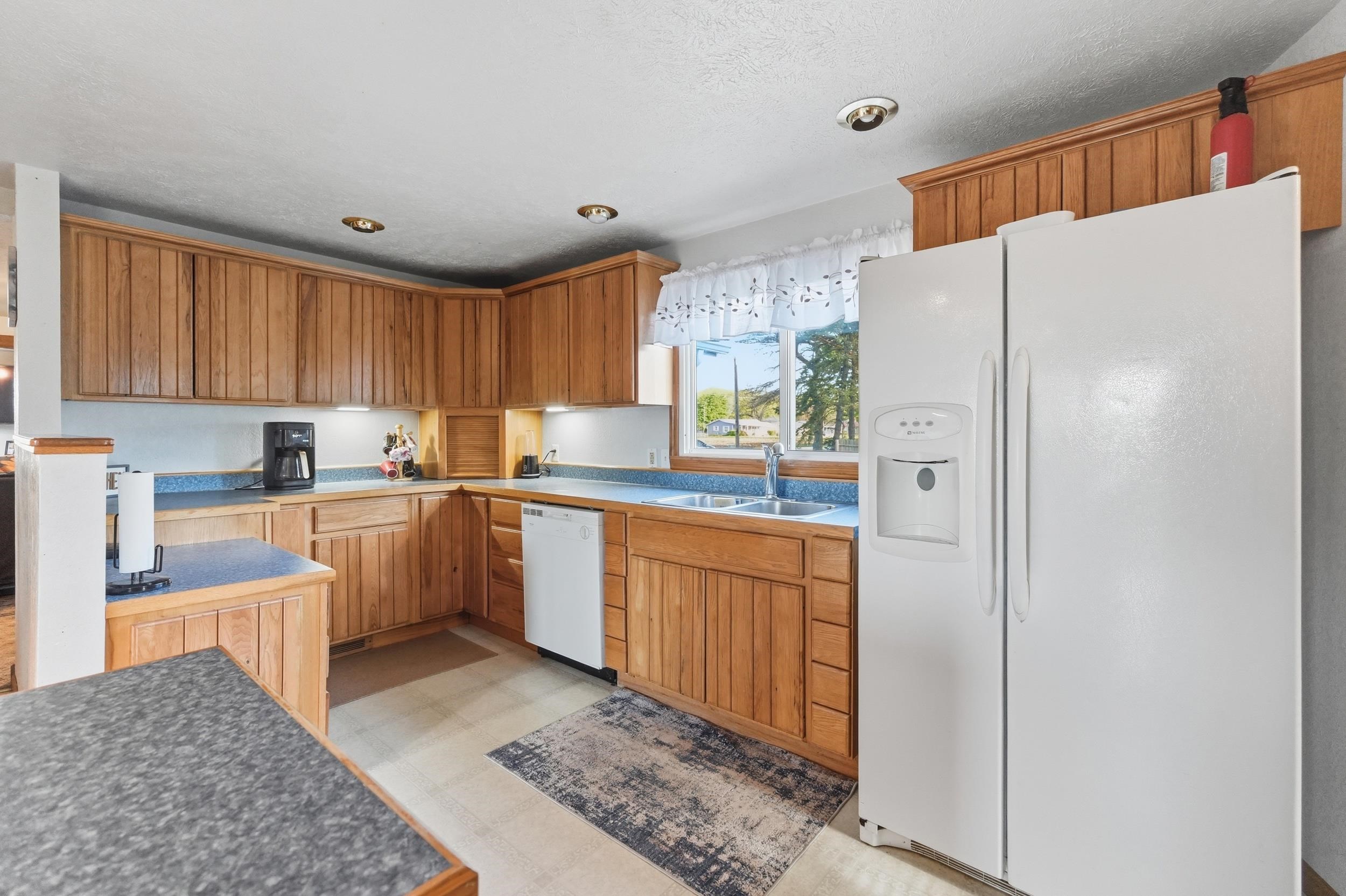 Kitchen featuring oak cabinetry, light-colored countertops, and integrated white appliances including a side-by-side refrigerator with ice and water dispenser