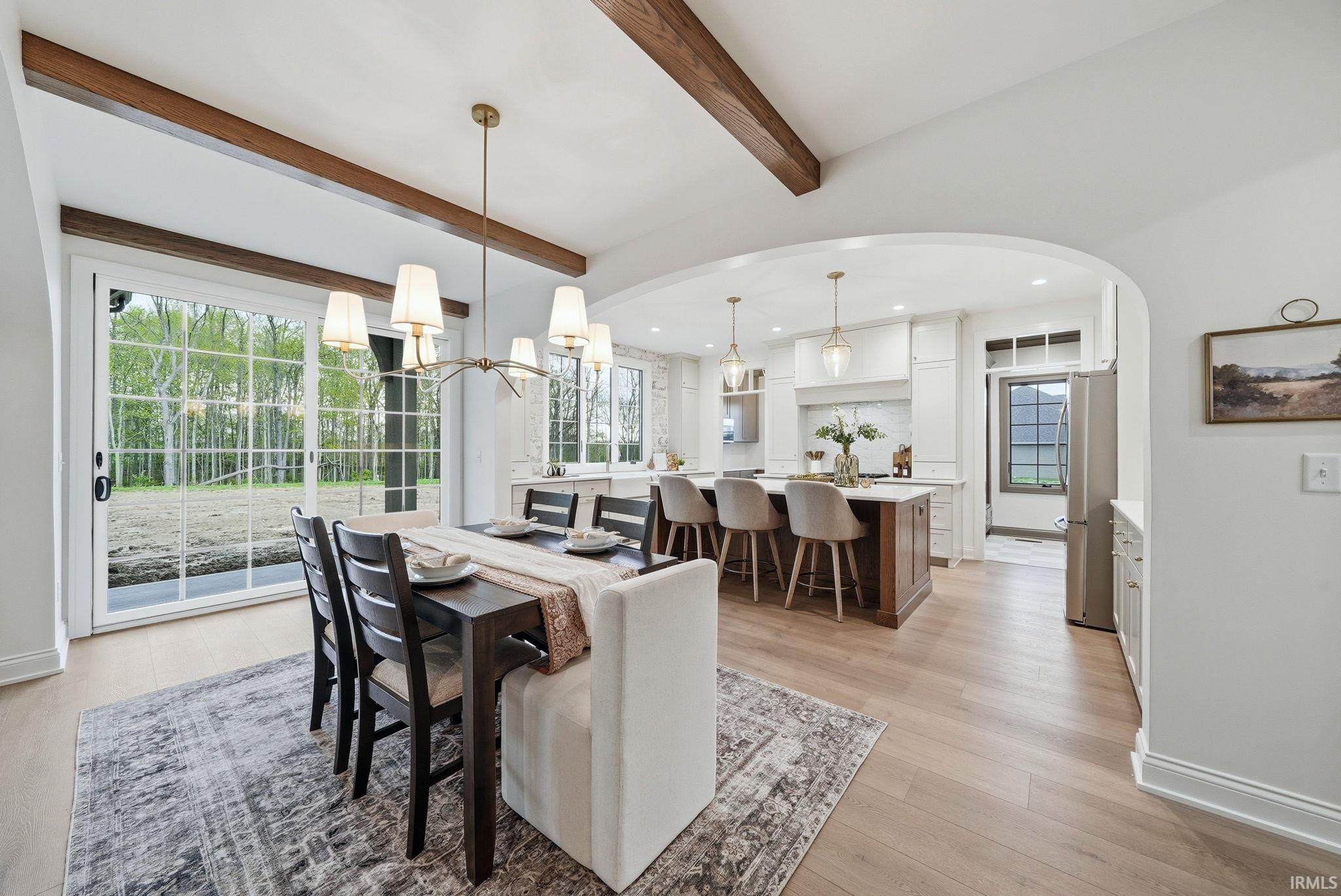 Spacious dining area featuring wood-finish flooring, exposed ceiling beams, and a modern chandelier