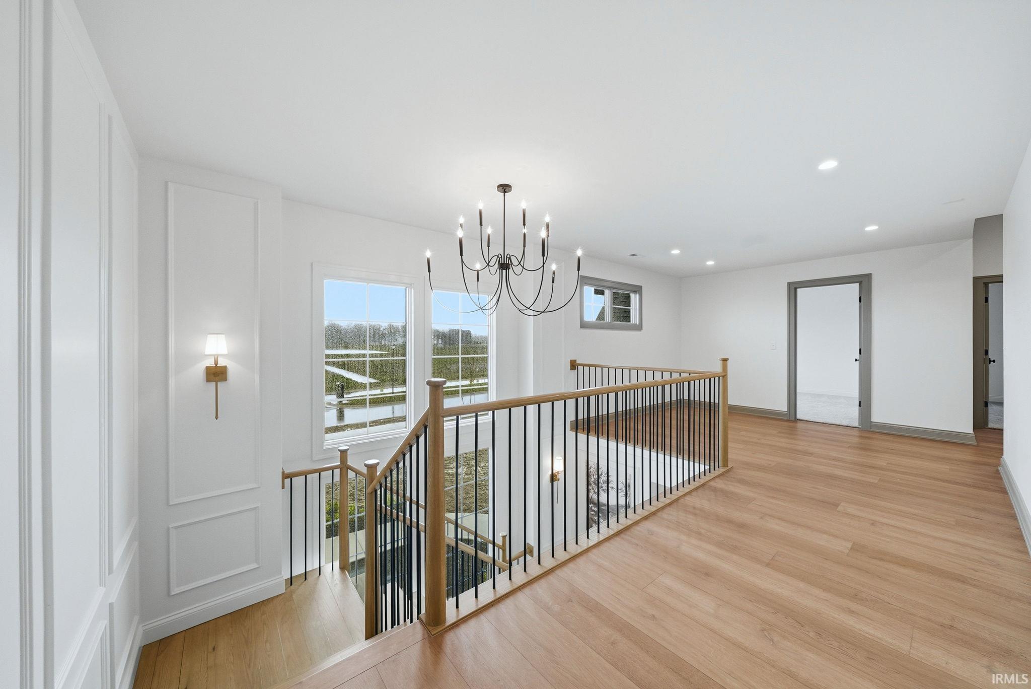 Upper-level landing featuring wood-finish flooring, a contemporary chandelier, recessed lighting, and a balustrade with wood railing and black iron spindles